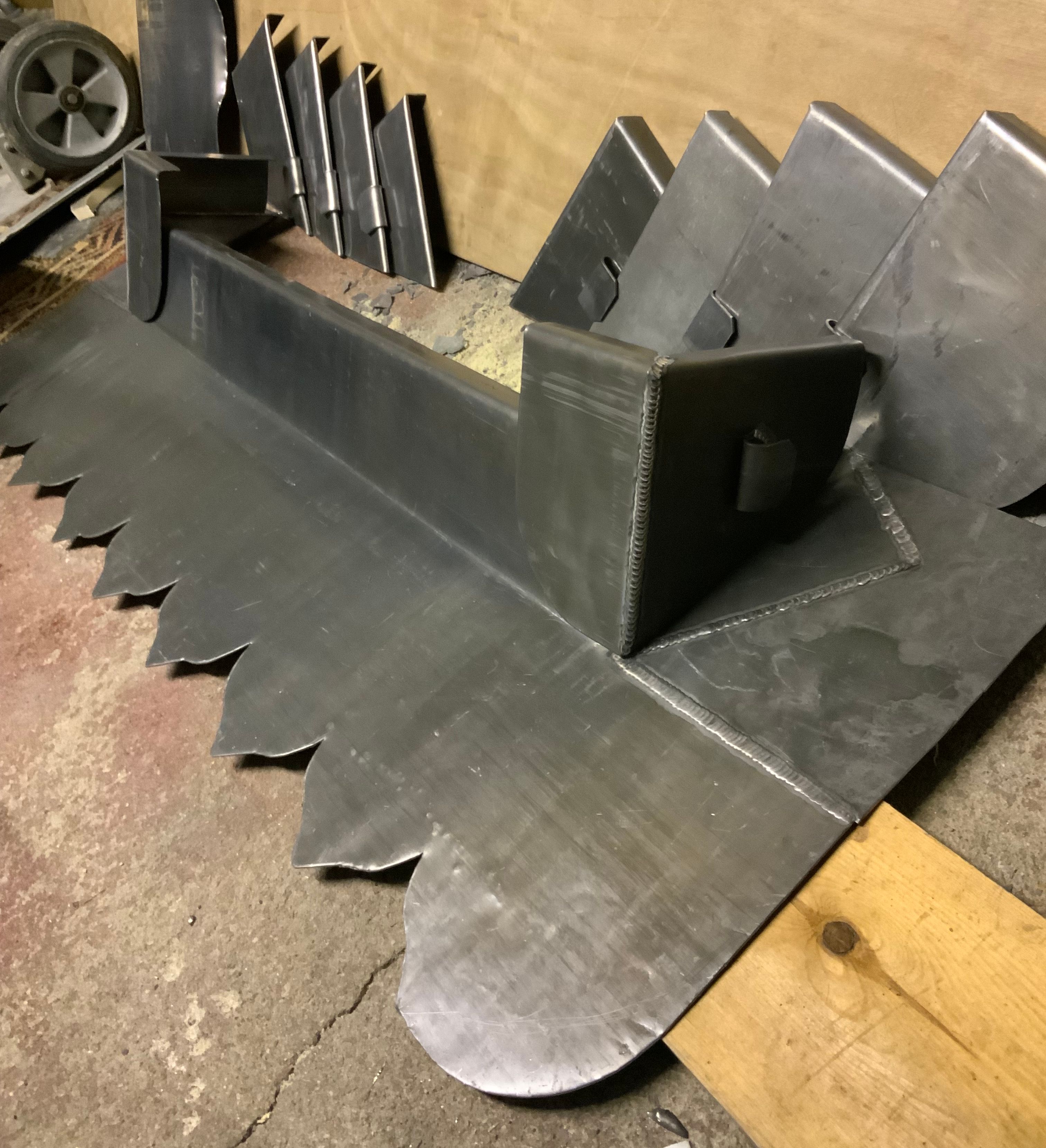 Assembled and cut metal parts, possibly for a large industrial or mechanical attachment, sitting on a workshop floor.