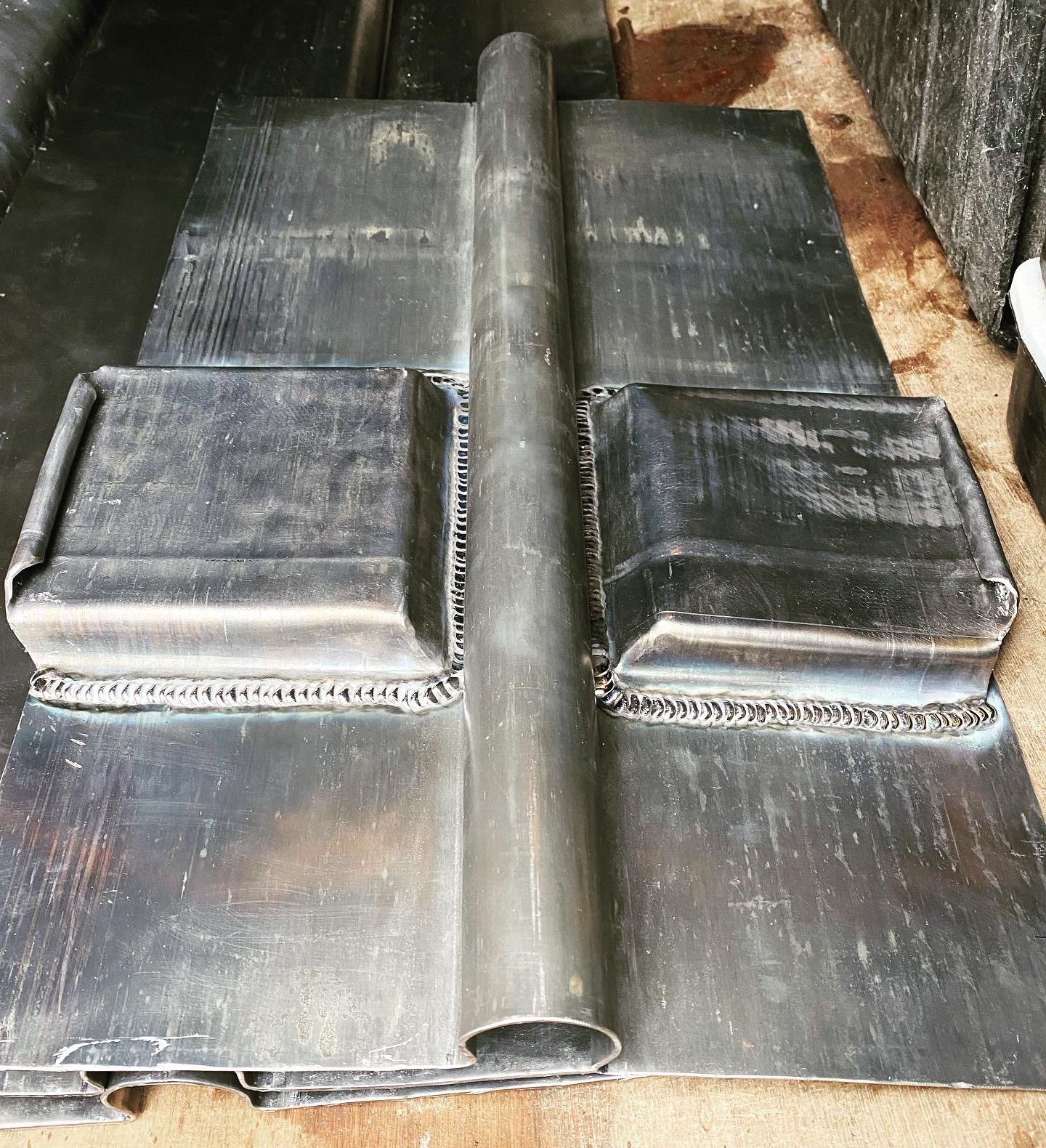 Welded sheet metal piece with two raised rectangular sections and a central cylindrical ridge