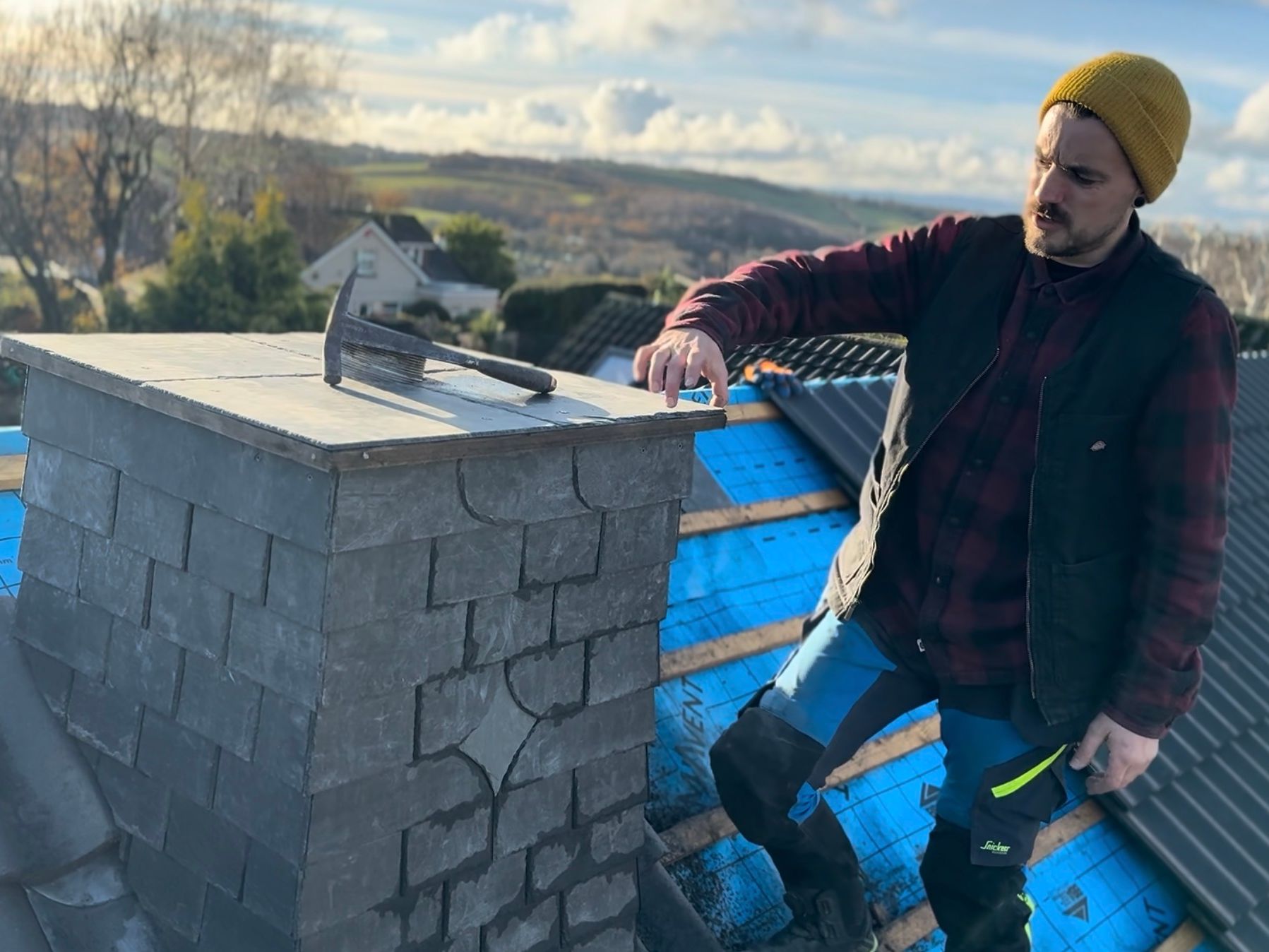 Roofer working on a chimney with tools on a house rooftop