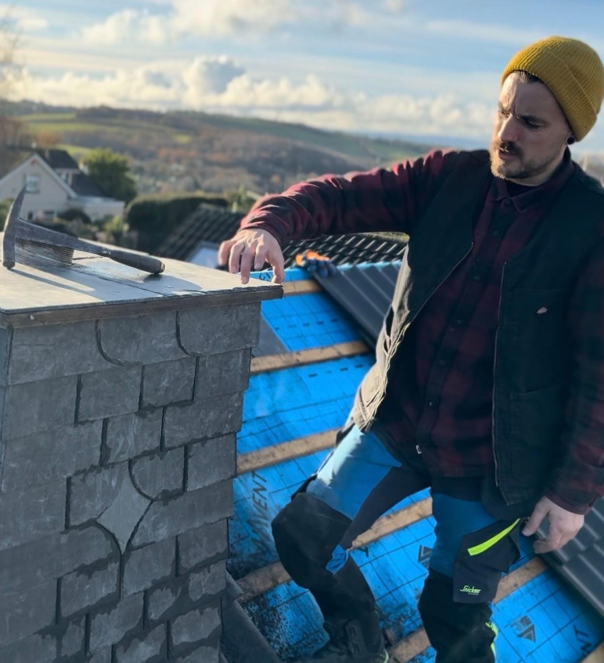 Roofer working on a chimney with tools on a house rooftop