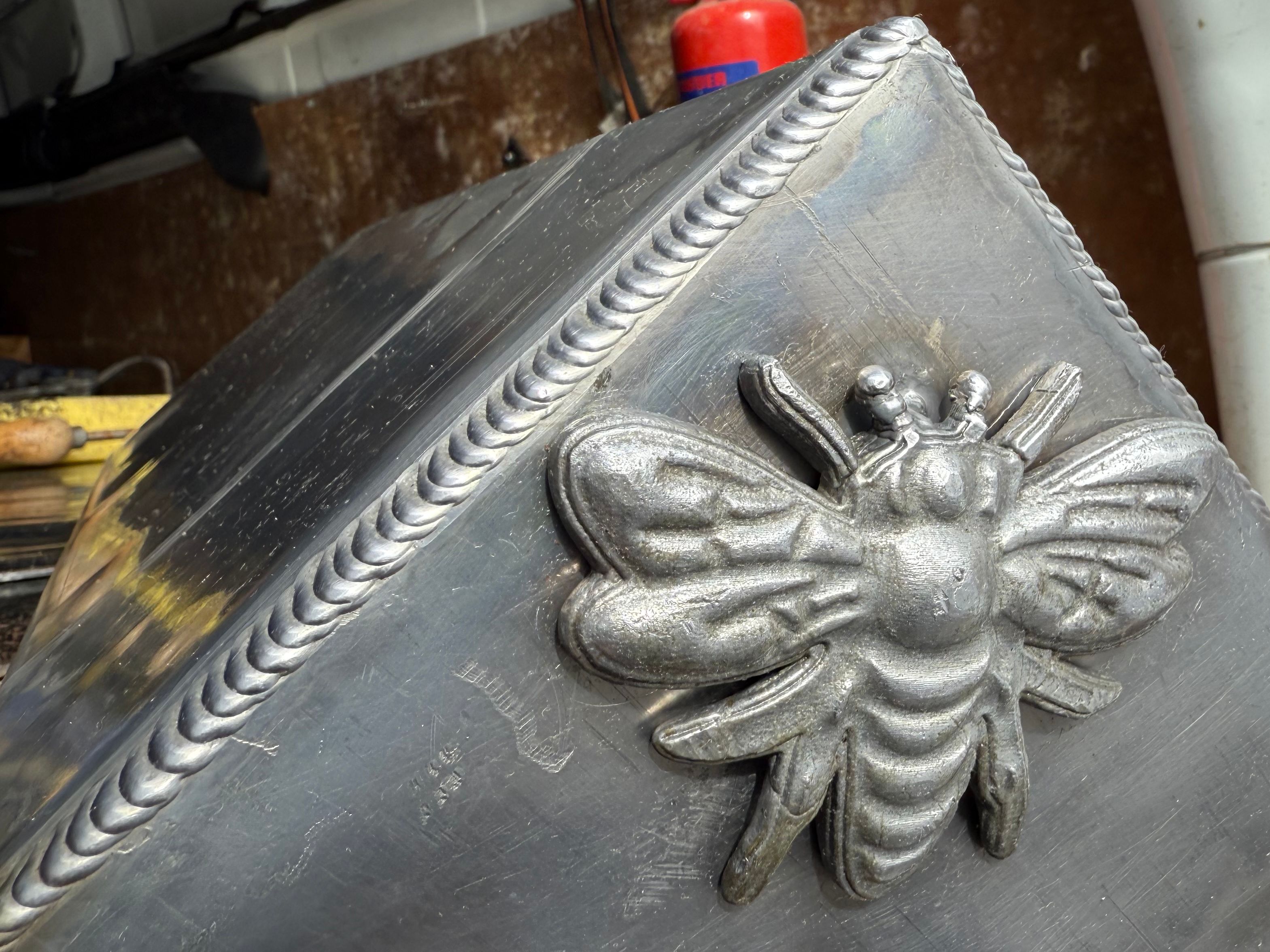 Close-up of a metallic bee sculpture welded onto a metal surface inside a vehicle.