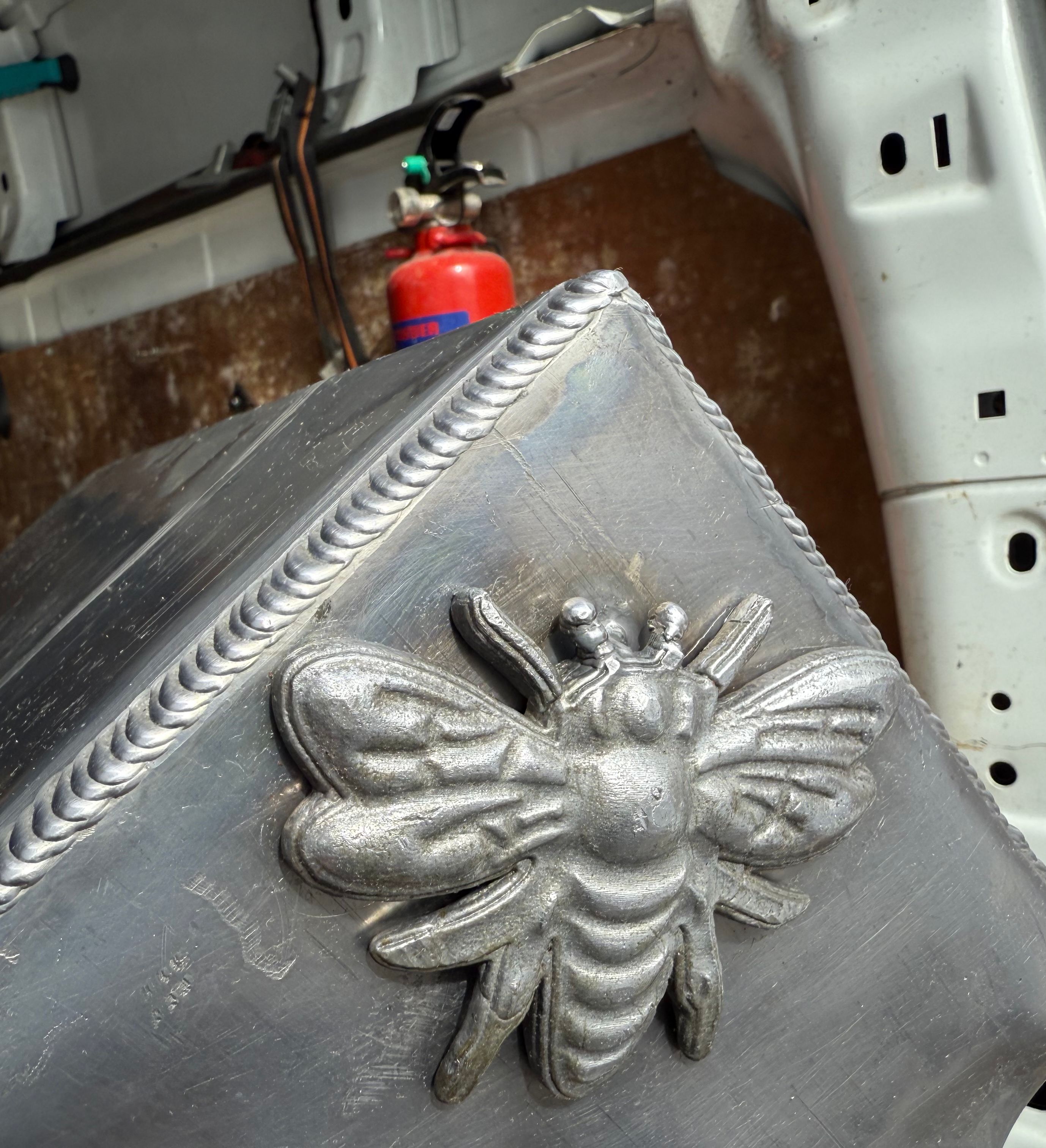 Close-up of a metallic bee sculpture welded onto a metal surface inside a vehicle.