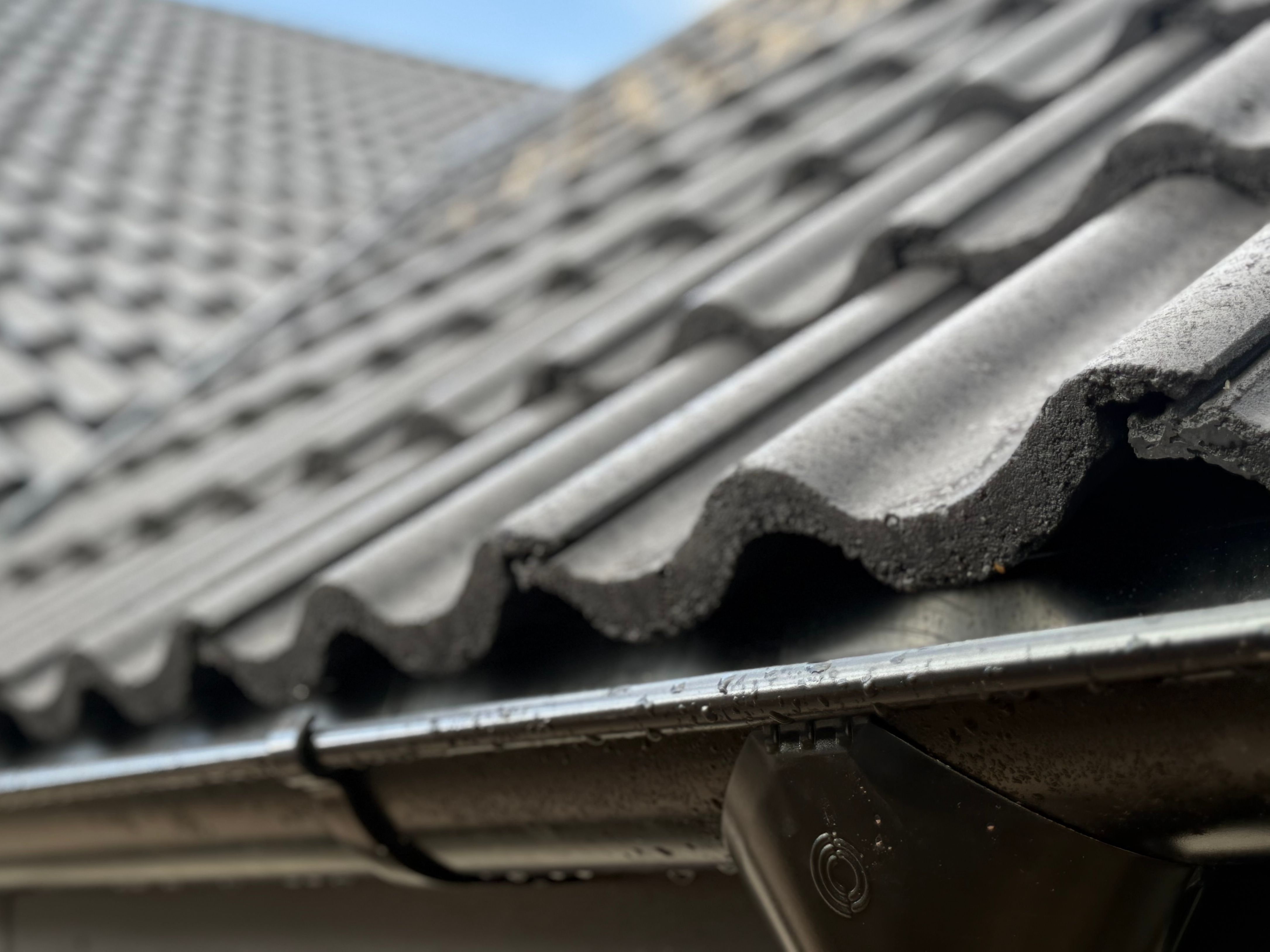 Close-up view of grey tiled roof with metal rain gutter.