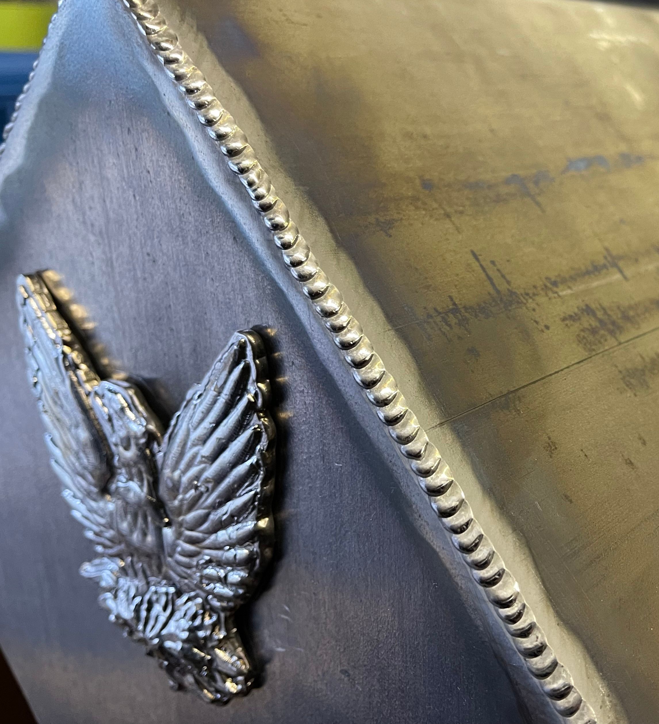 Close-up of a welded metal object with an embossed eagle symbol in a workshop setting.