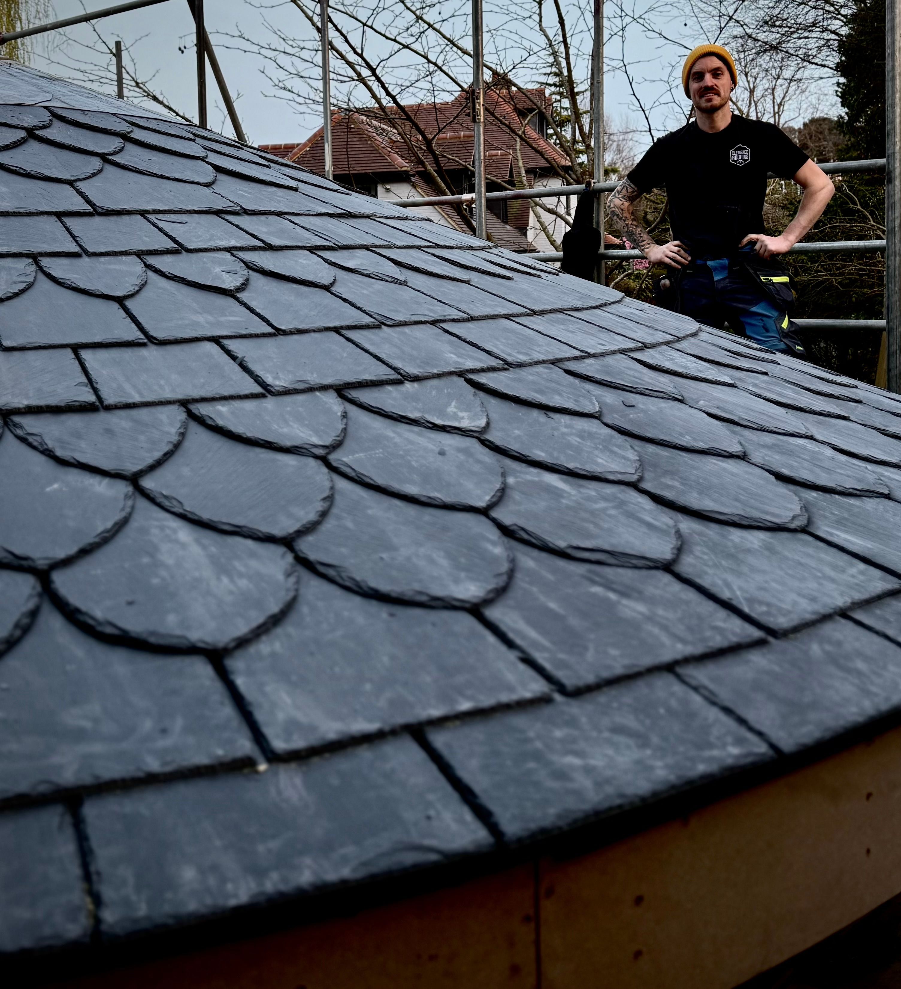 Person standing next to a round slate-tiled roof structure on a construction site