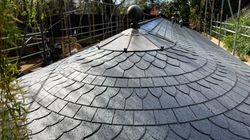 Curved slate roof with metal detailing and raindrops, surrounded by scaffolding and trees.
