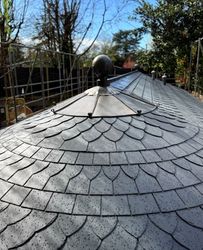 Curved slate roof with metal detailing and raindrops, surrounded by scaffolding and trees.