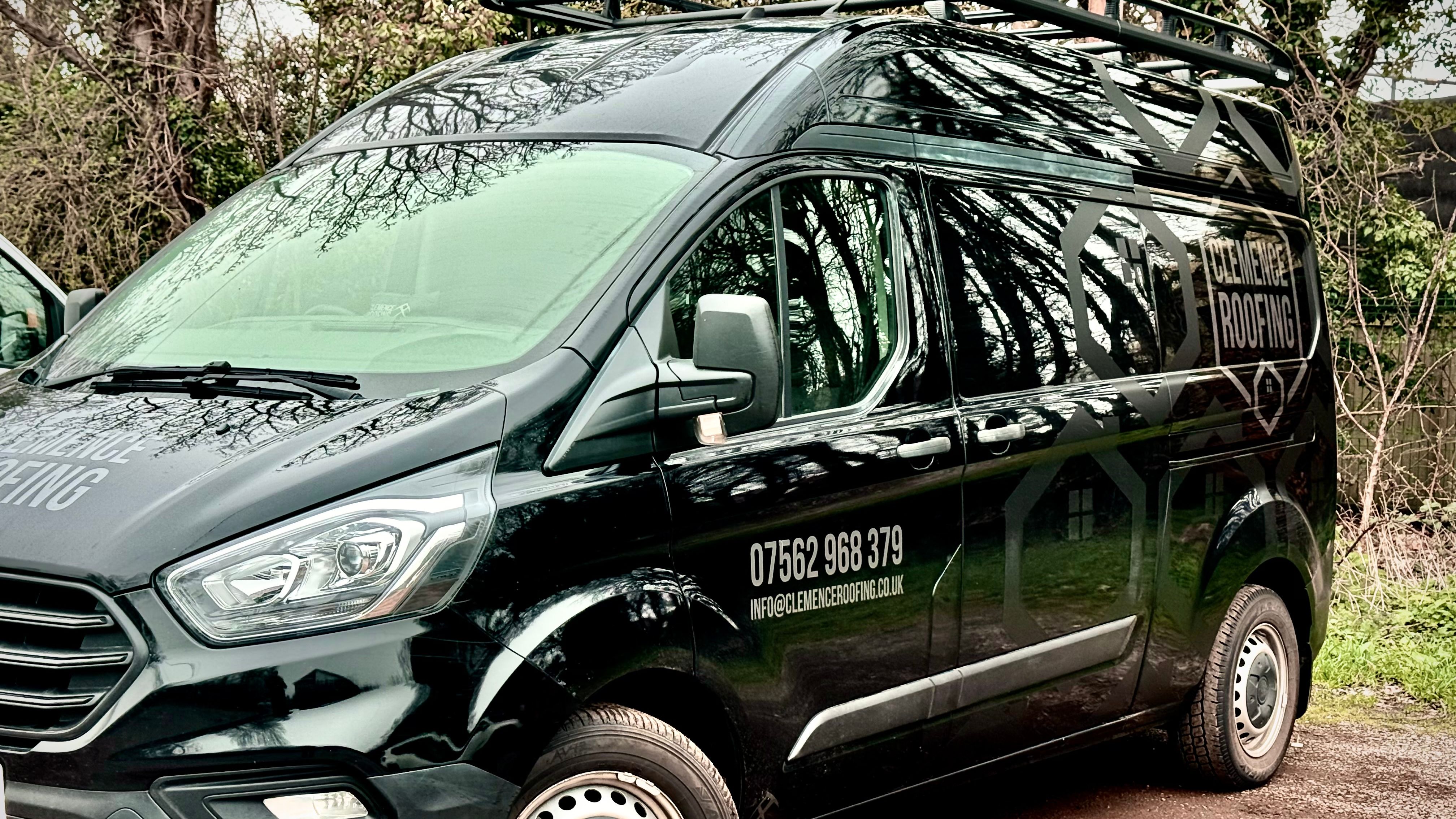 Black Clemence Roofing van parked on a dirt driveway near trees.