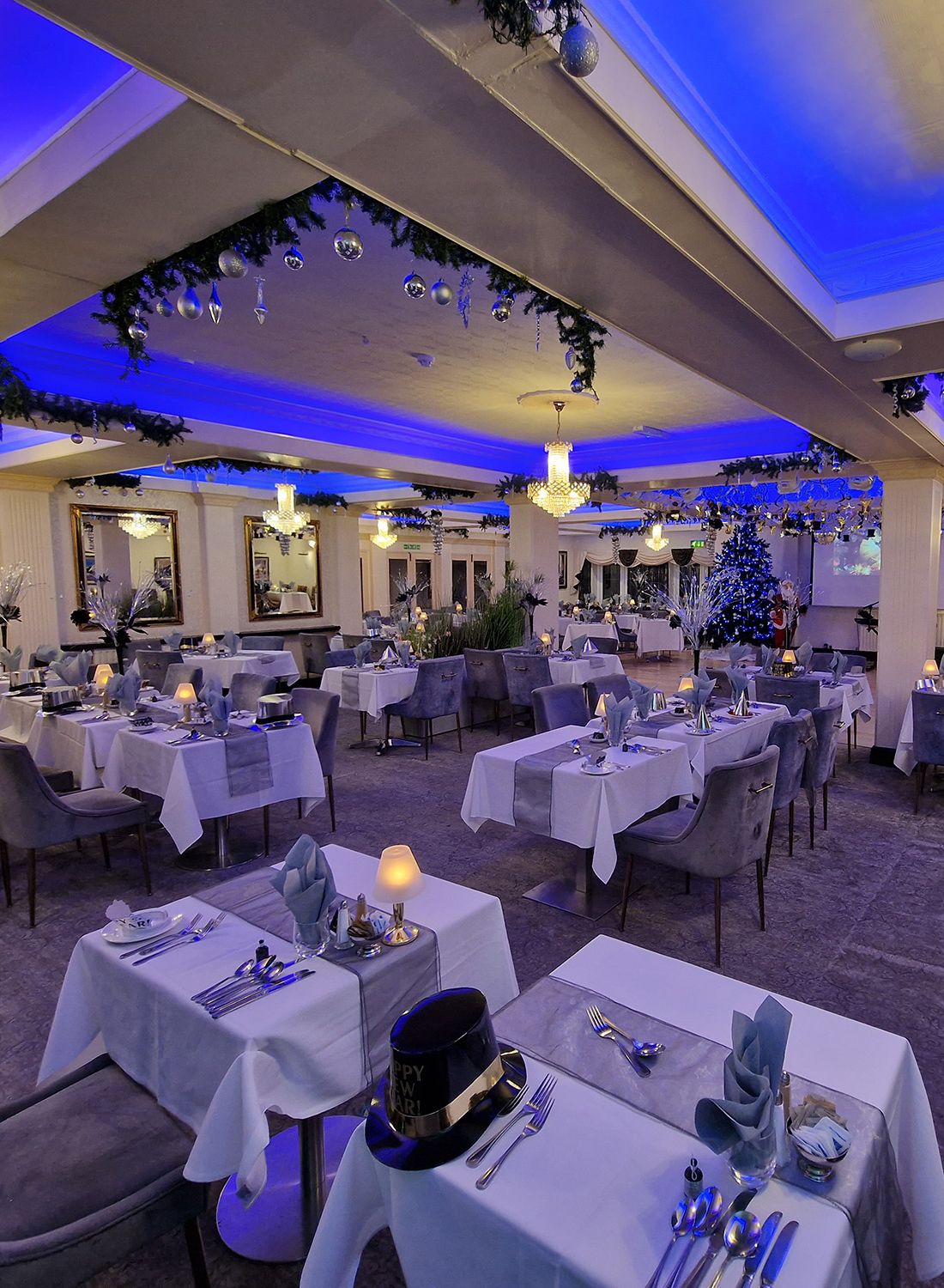 Elegant restaurant dining room with white tablecloths, chandeliers and blue ambient lighting, decorated for New Year