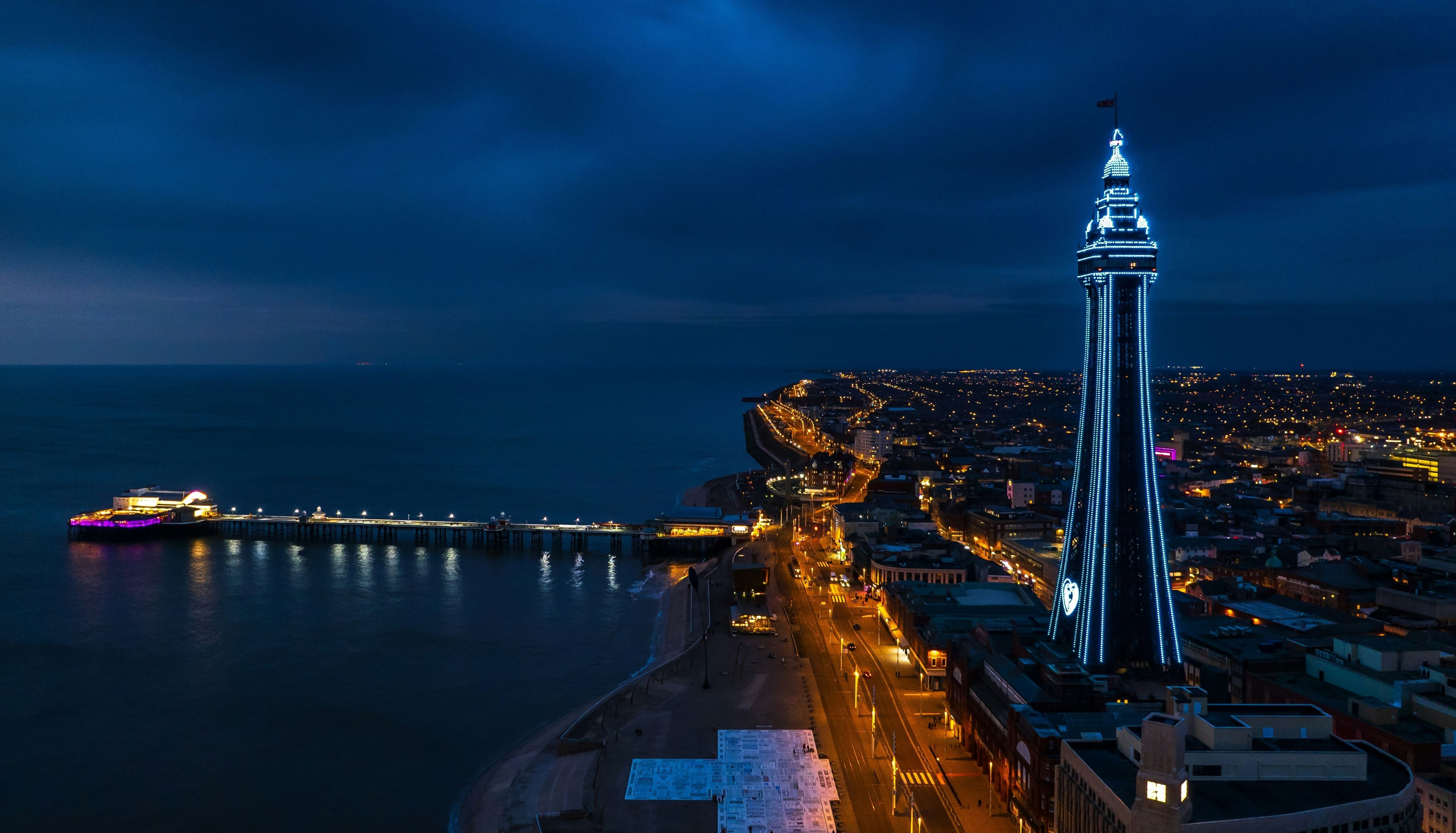 Night-time aerial view of Blackpool Tower illuminated in blue beside the seafront and pier