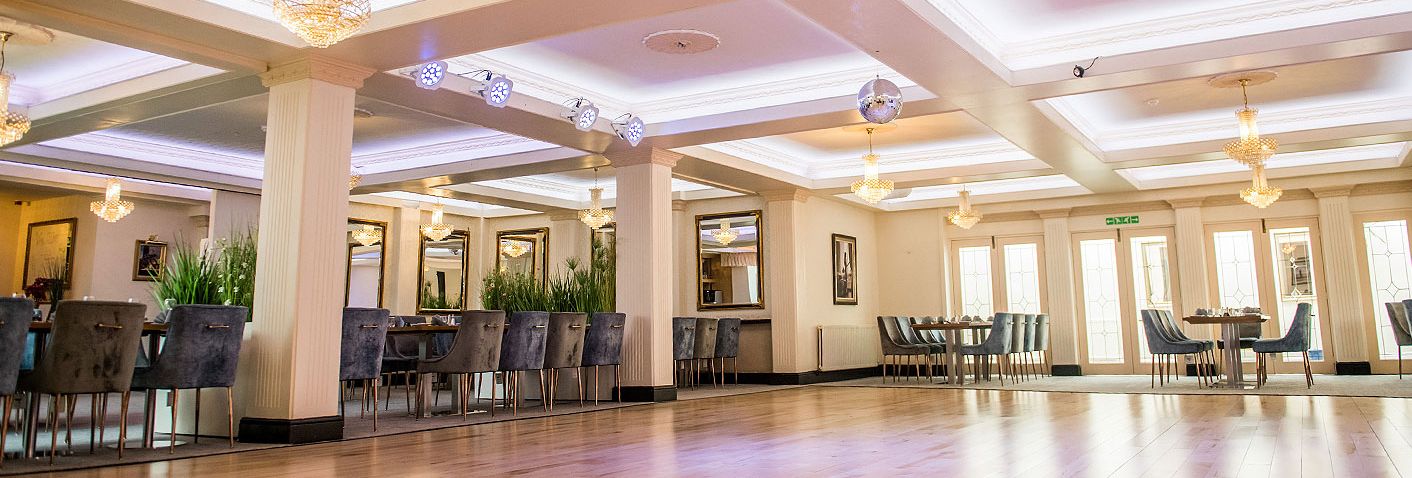 Spacious function room with wooden dance floor, chandeliers and dining tables
