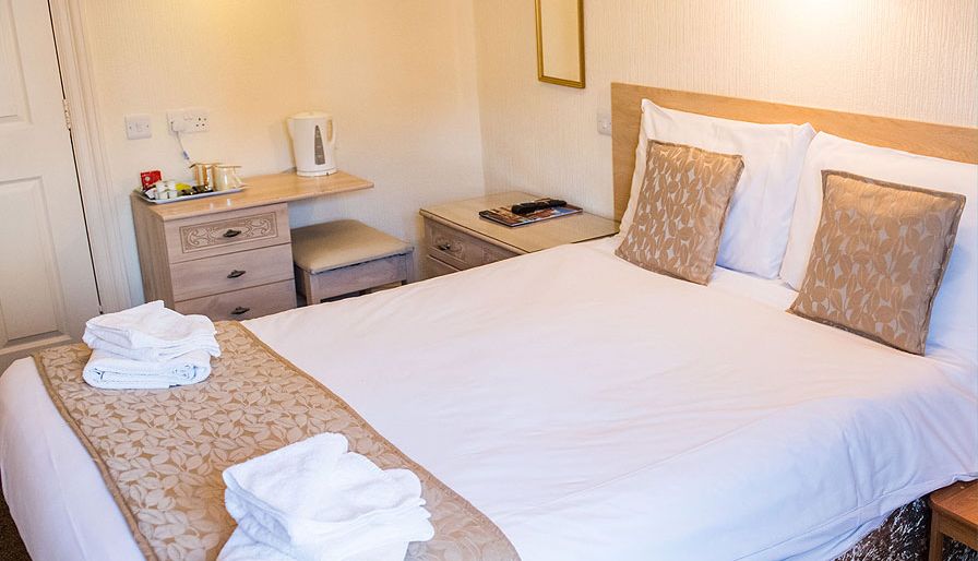 Cosy double bedroom with white bedding, patterned cushions and a small desk with kettle
