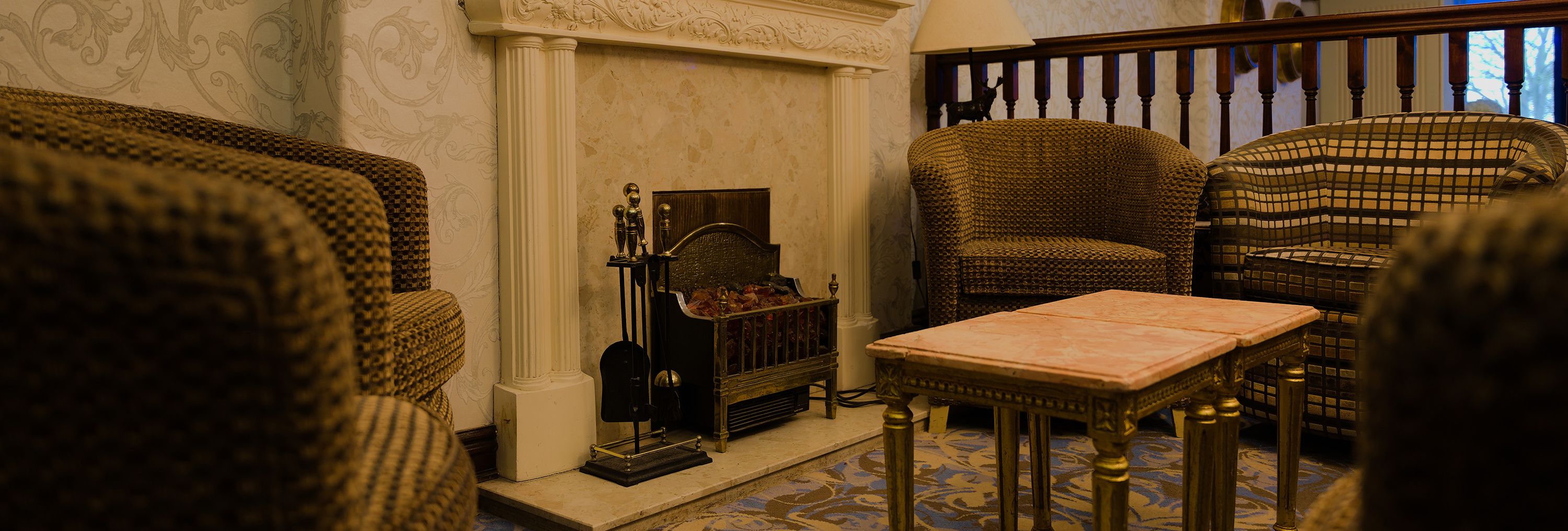 Cosy lounge area with ornate fireplace, patterned armchairs and a small table