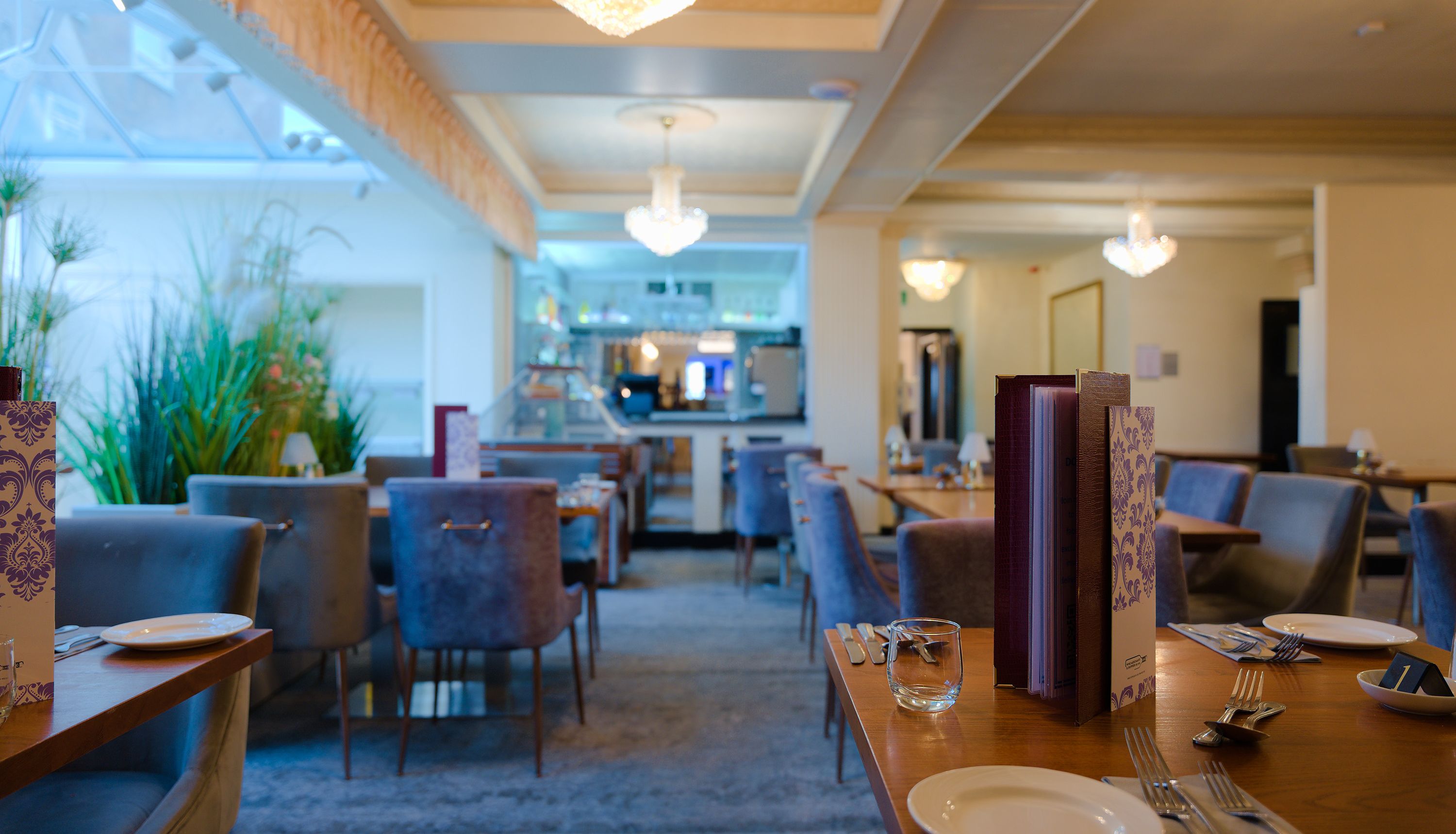 Cosy restaurant dining room with set tables, upholstered chairs and chandeliers