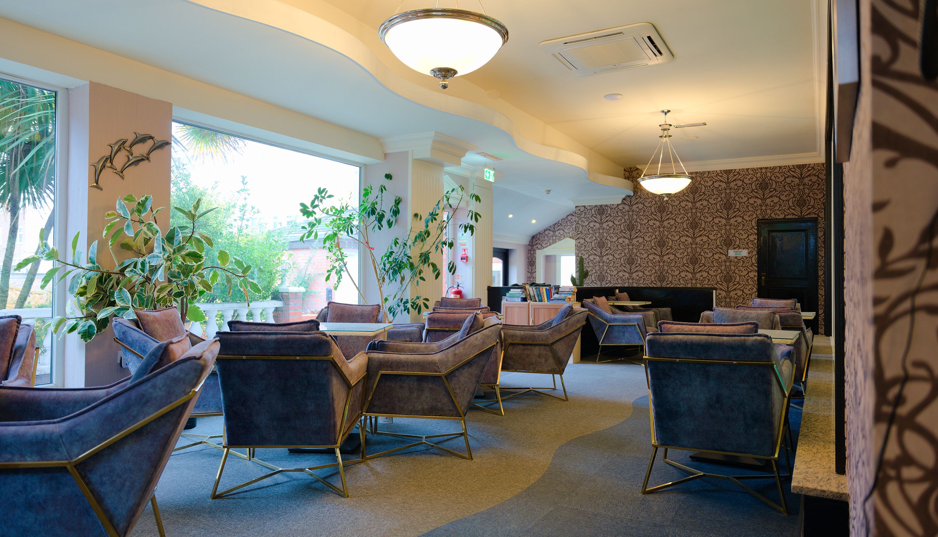 Hotel lounge seating area with blue velvet armchairs, large windows and pendant lights