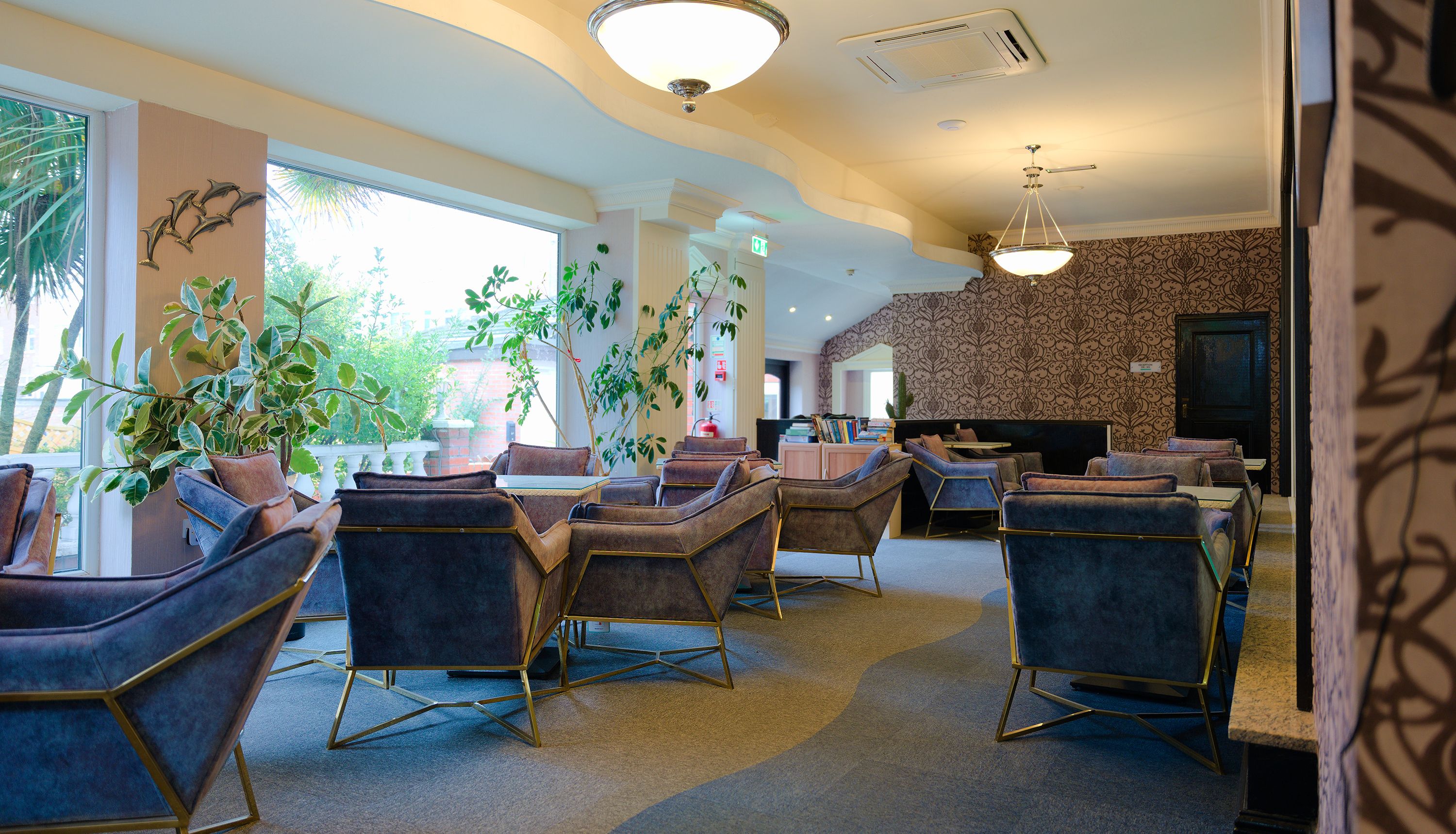 Hotel lounge seating area with blue velvet armchairs, large windows and pendant lights