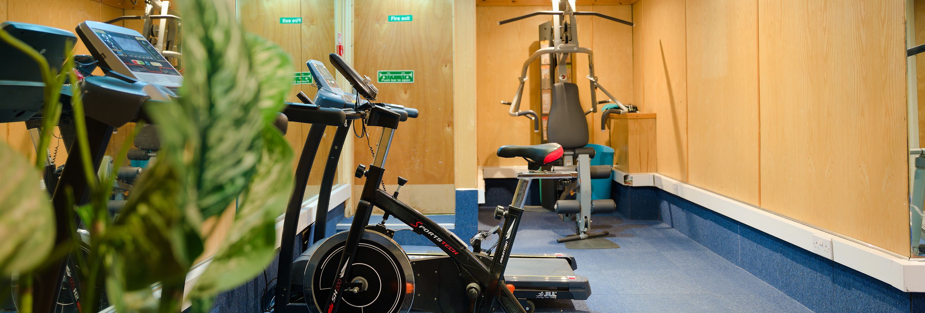 Small gym room with exercise bike, treadmill and multi-gym machine beside mirrored wall