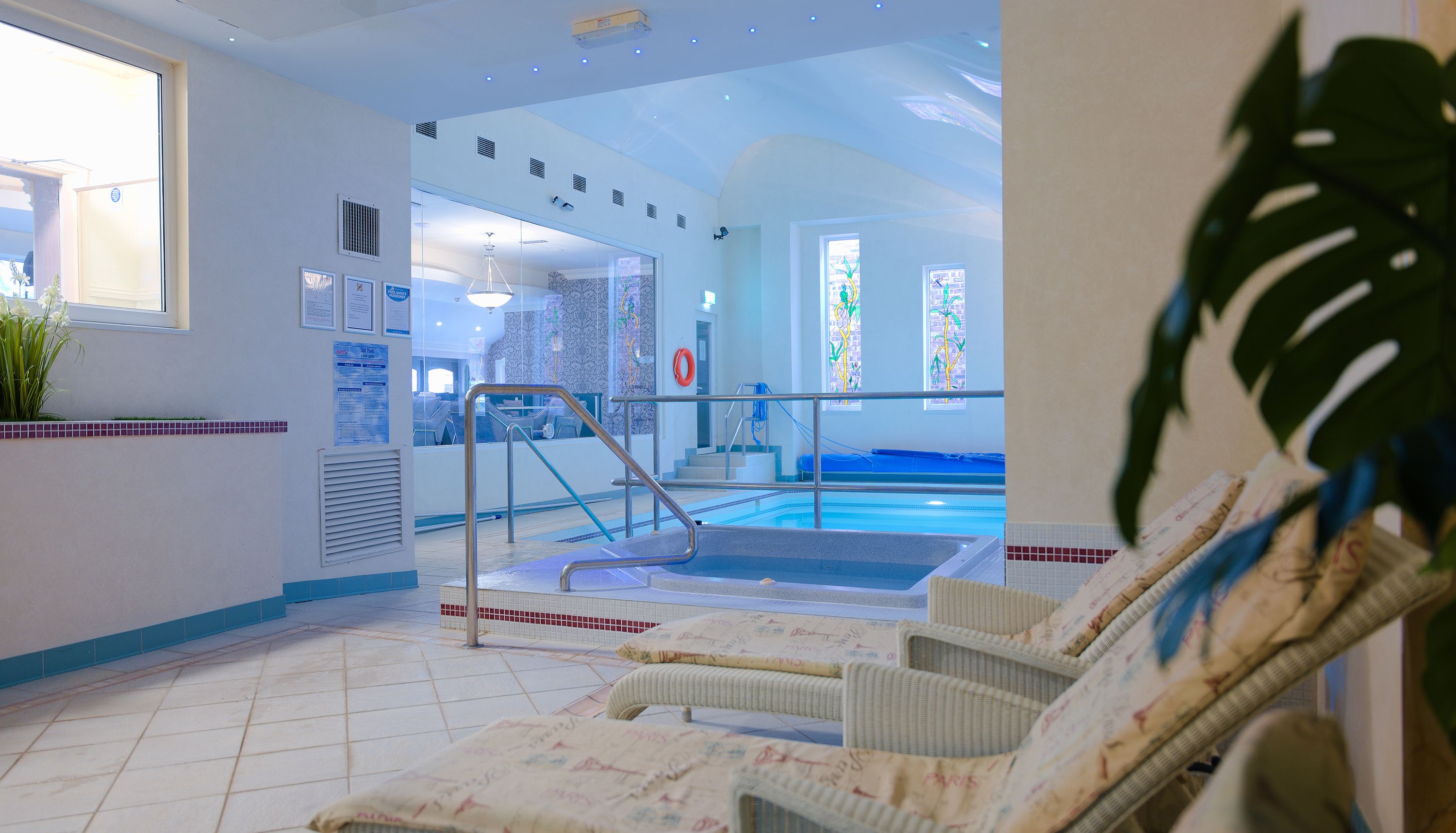 Indoor swimming pool and hot tub with tiled floor, metal handrails and loungers