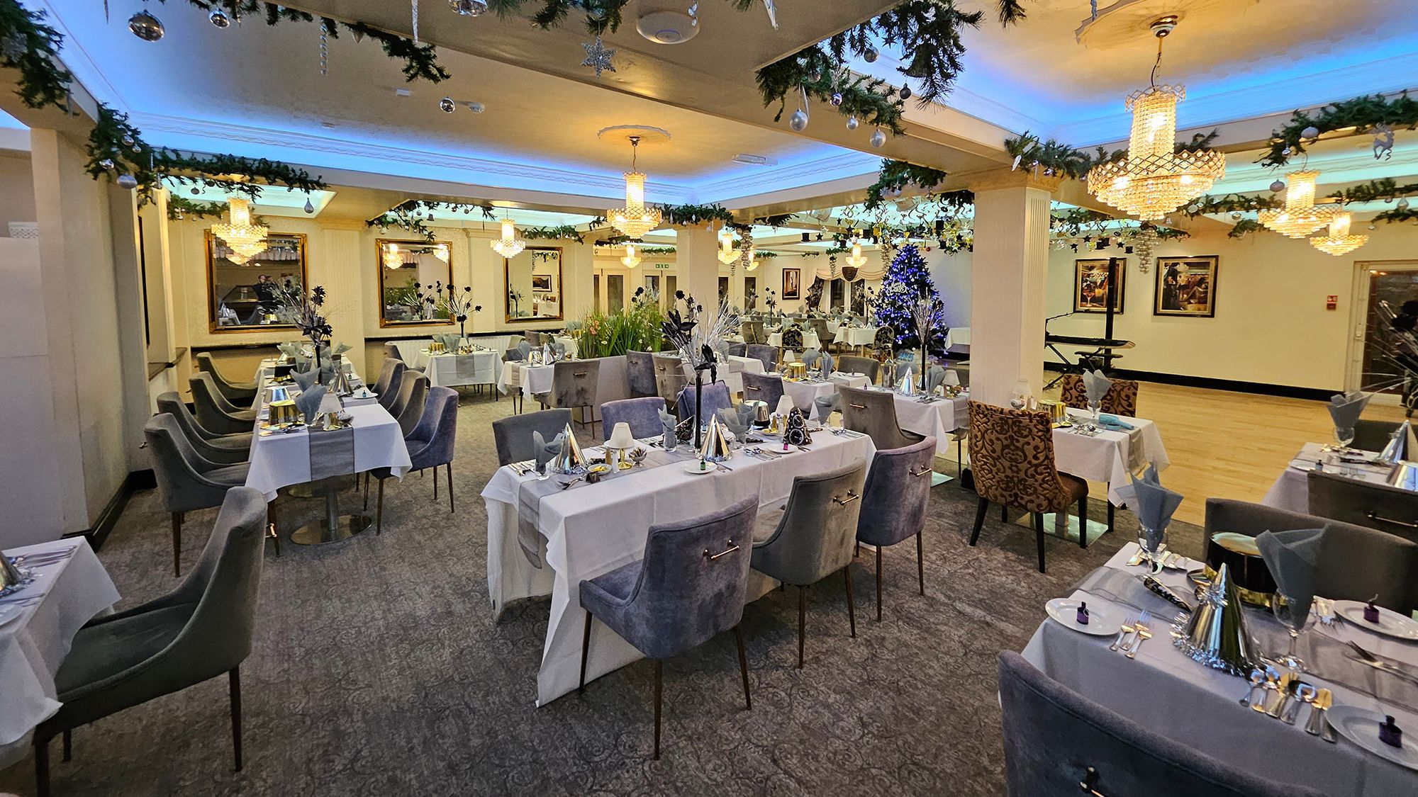 Festively decorated dining room with garlands, baubles and chandeliers above set tables