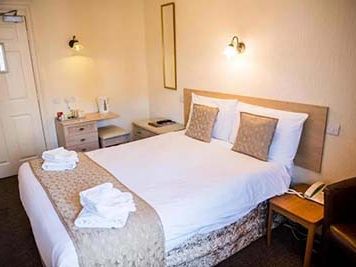 Double bed in a small hotel room with bedside tables and folded towels