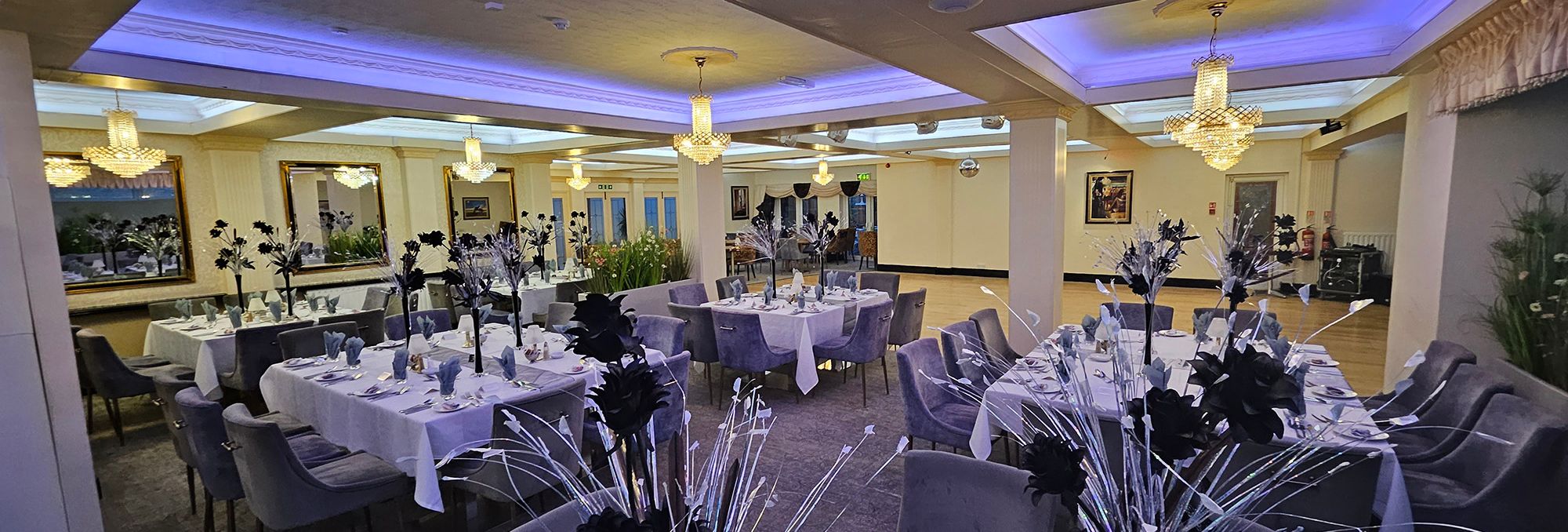 Banquet hall set for a formal event with white tablecloths, black floral centrepieces and crystal chandeliers