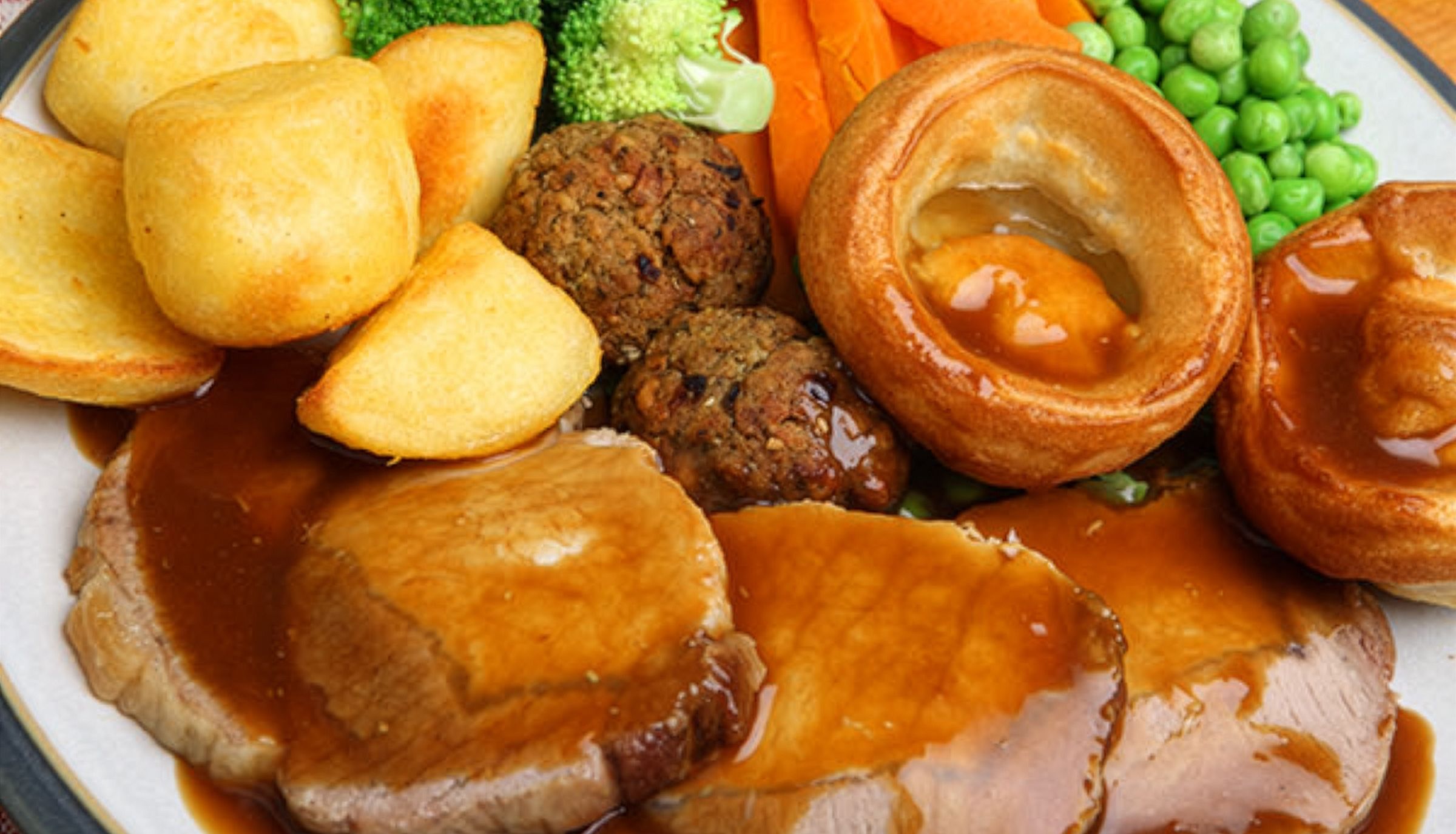 Traditional Sunday roast dinner with sliced meat, roast potatoes, Yorkshire puddings, broccoli, carrots, peas and gravy