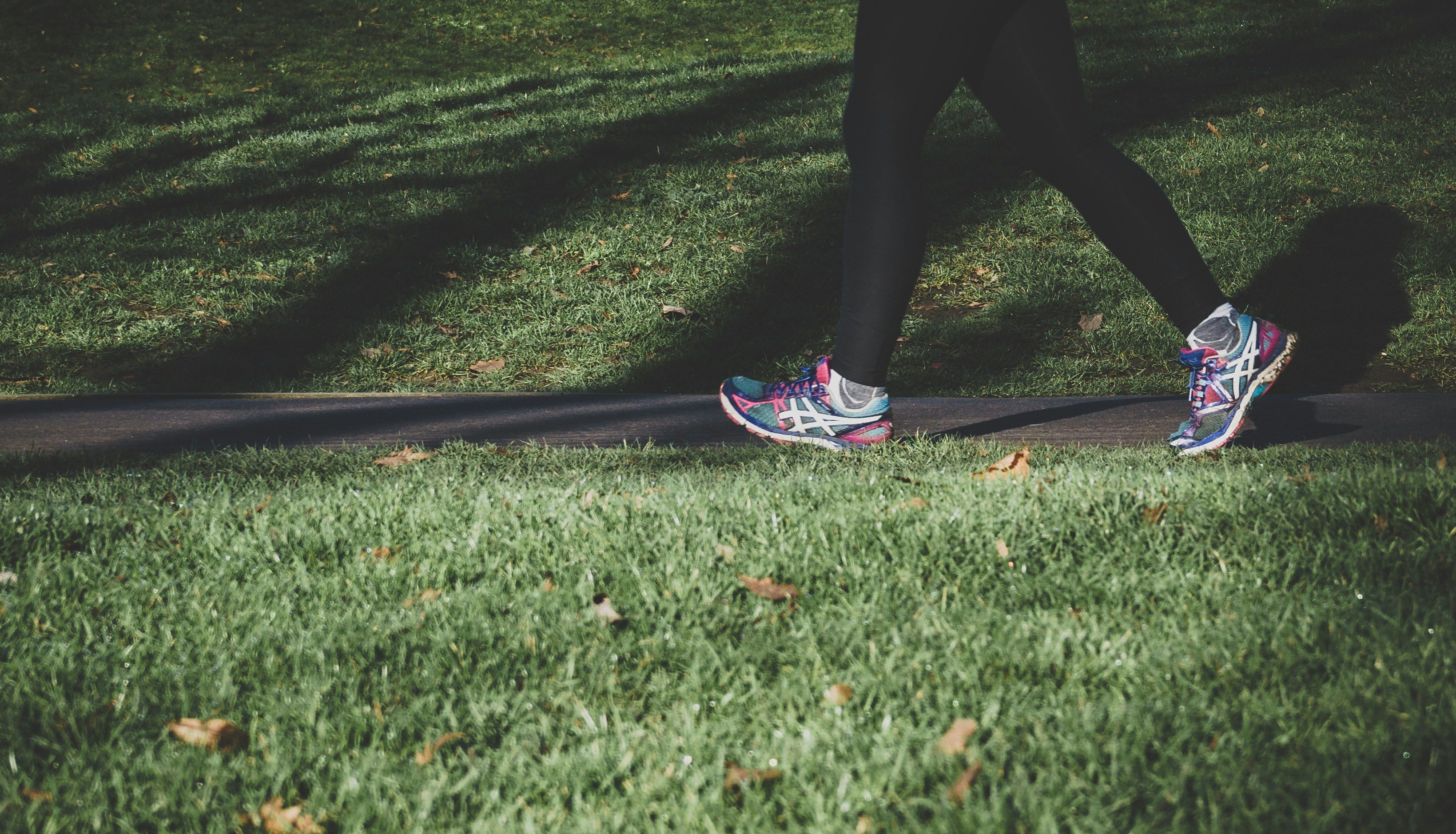 Person walking along a park path wearing colourful running trainers