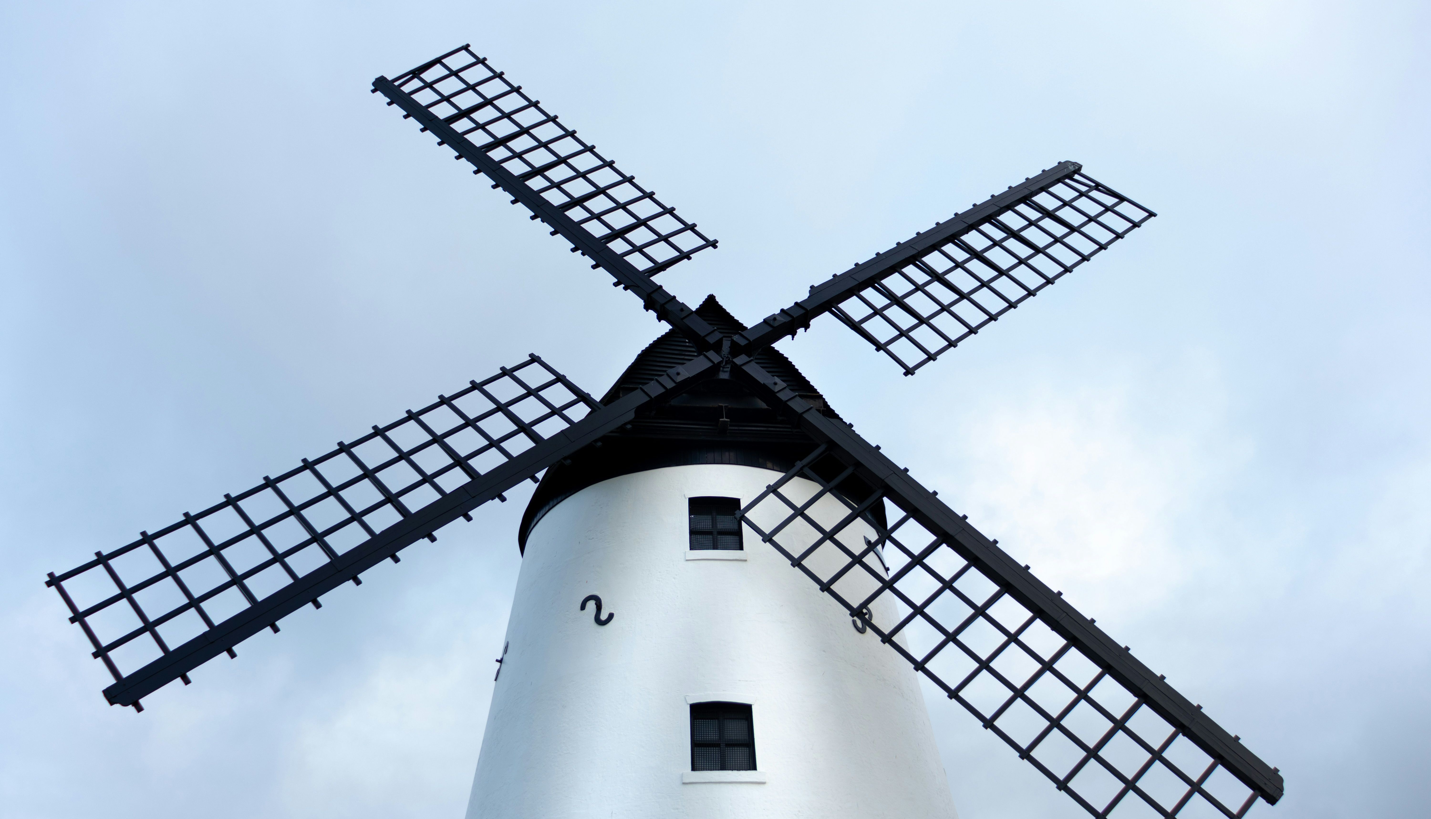 Low-angle view of a white windmill with black sails against a pale blue sky