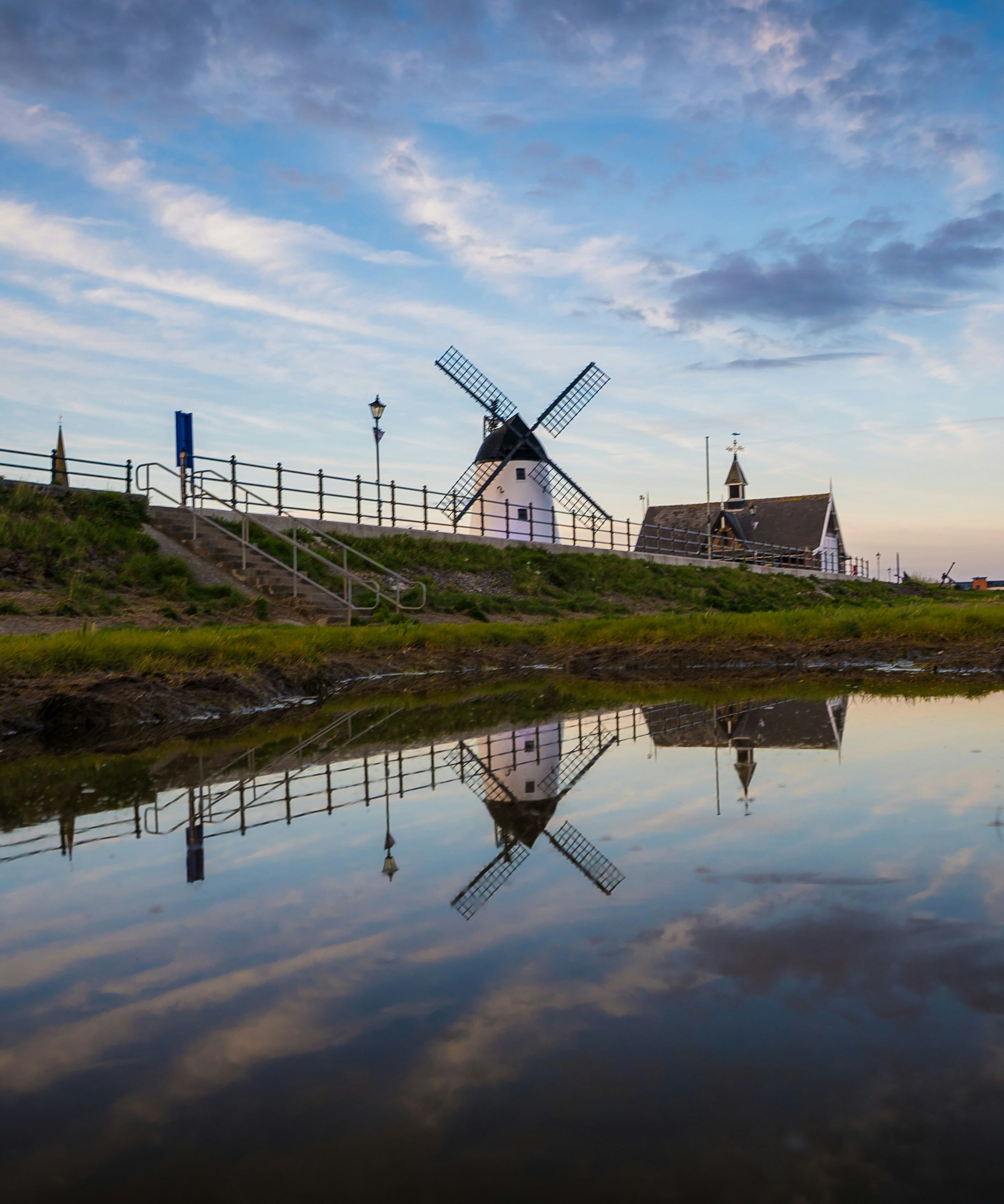 Windmill on a grassy embankment reflected in calm water at dusk