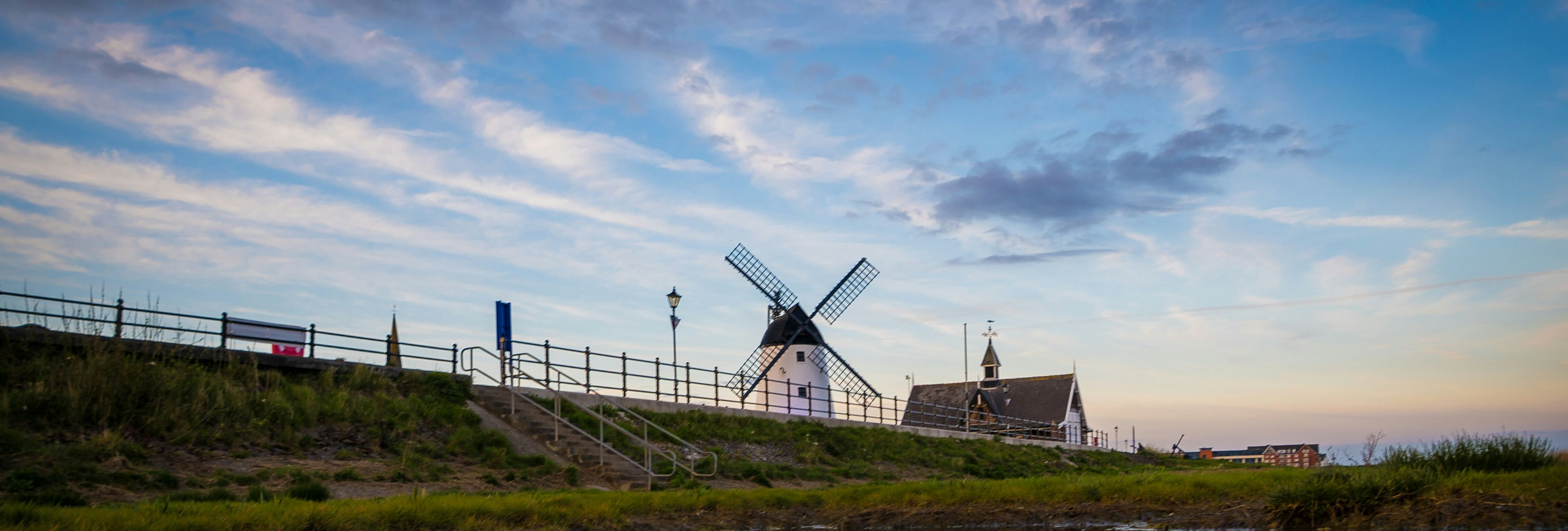 Windmill on a grassy embankment reflected in calm water at dusk