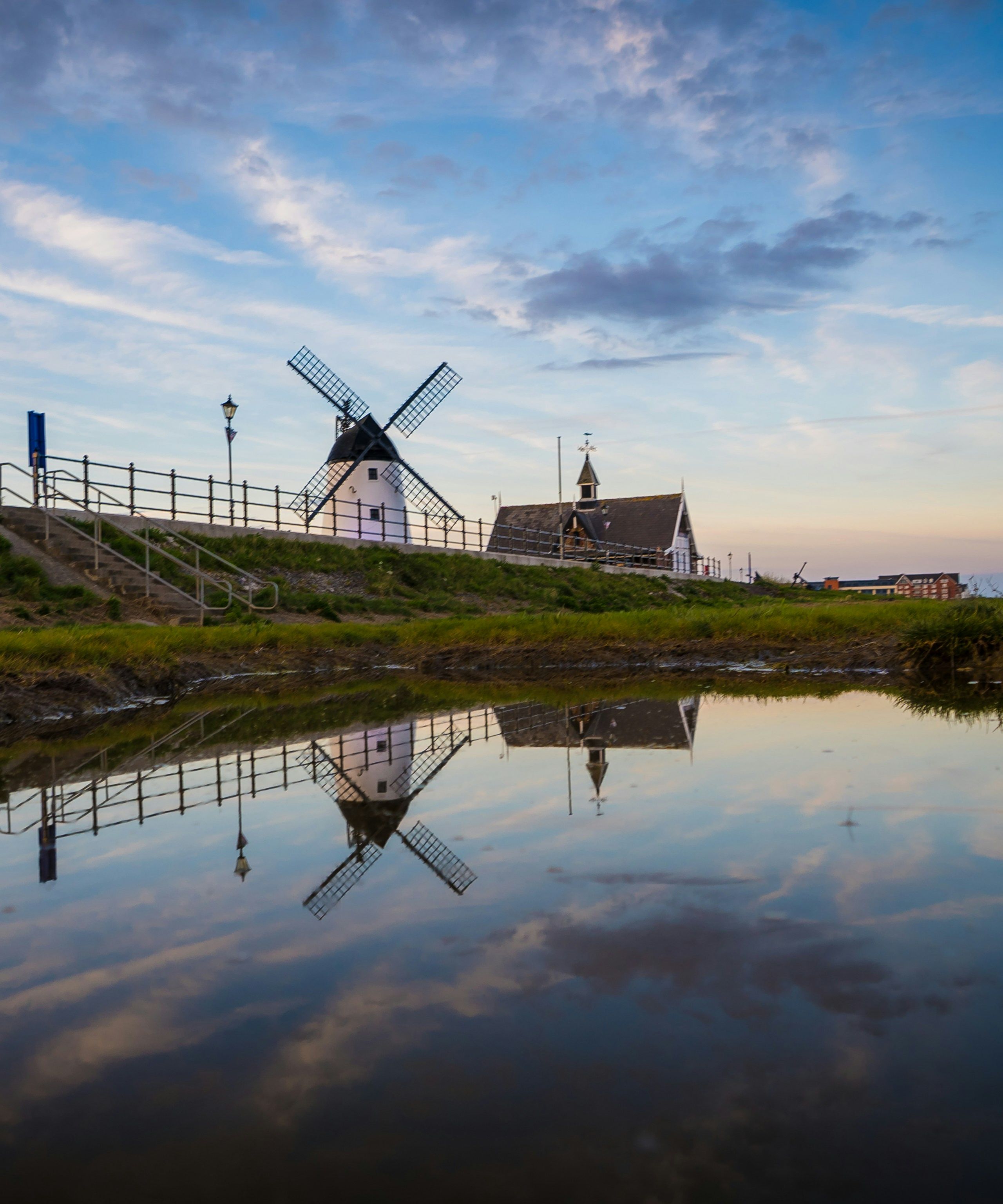 Windmill on a grassy embankment reflected in calm water at dusk
