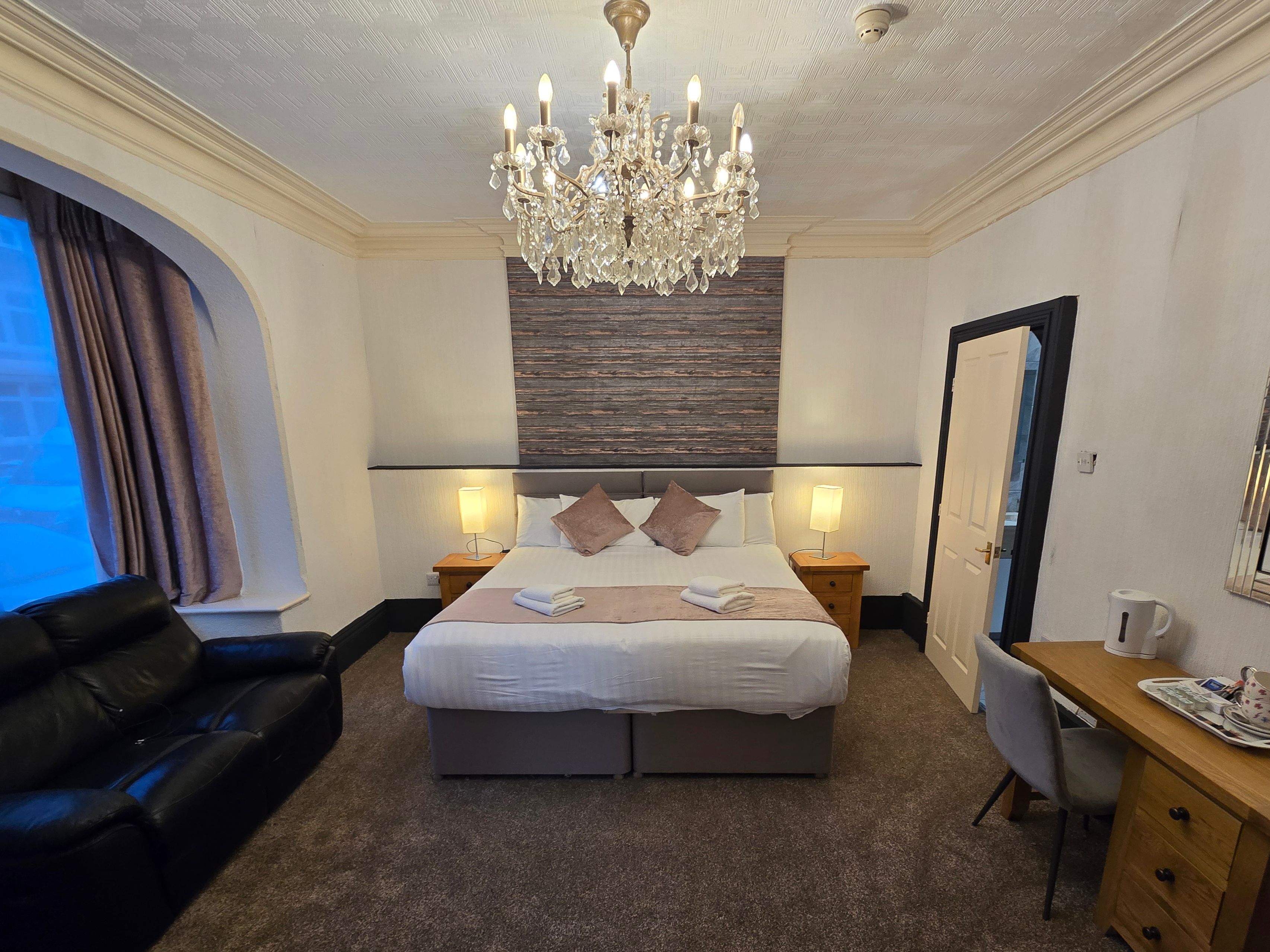 Cosy hotel bedroom with double bed, crystal chandelier, black leather sofa and wooden desk