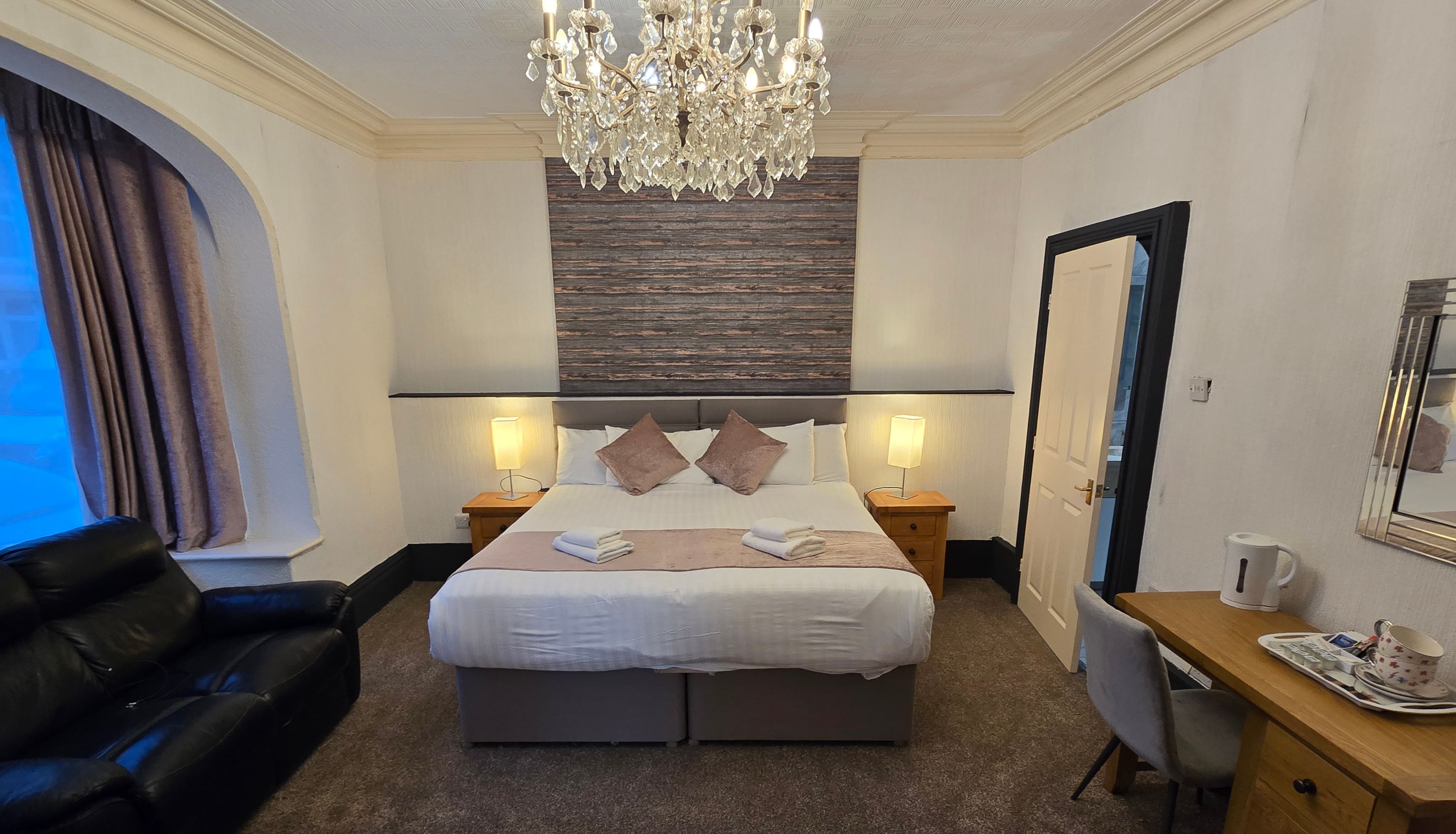Cosy hotel bedroom with double bed, crystal chandelier, black leather sofa and wooden desk