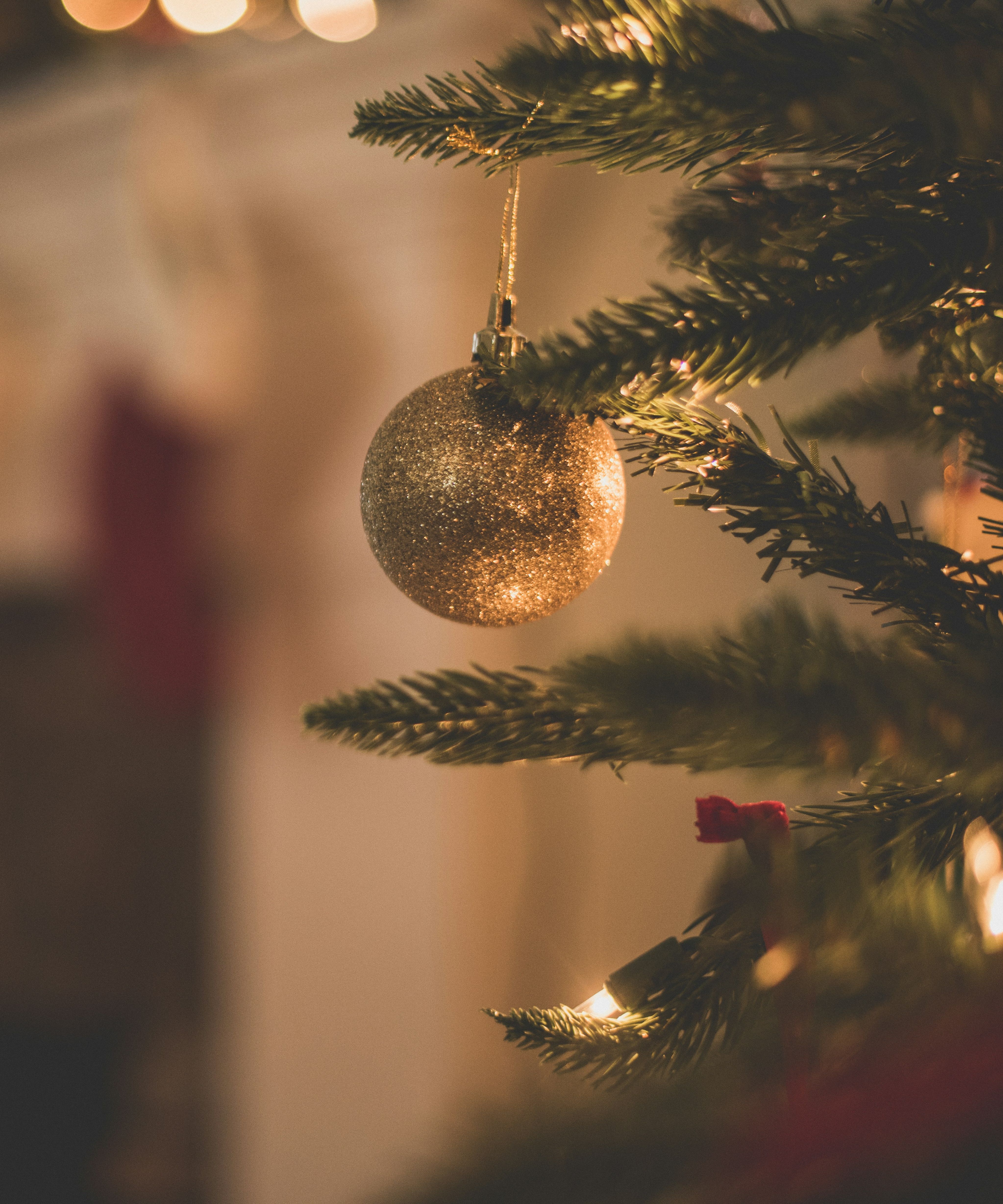 Gold glitter bauble hanging on a Christmas tree with warm fairy lights in the background