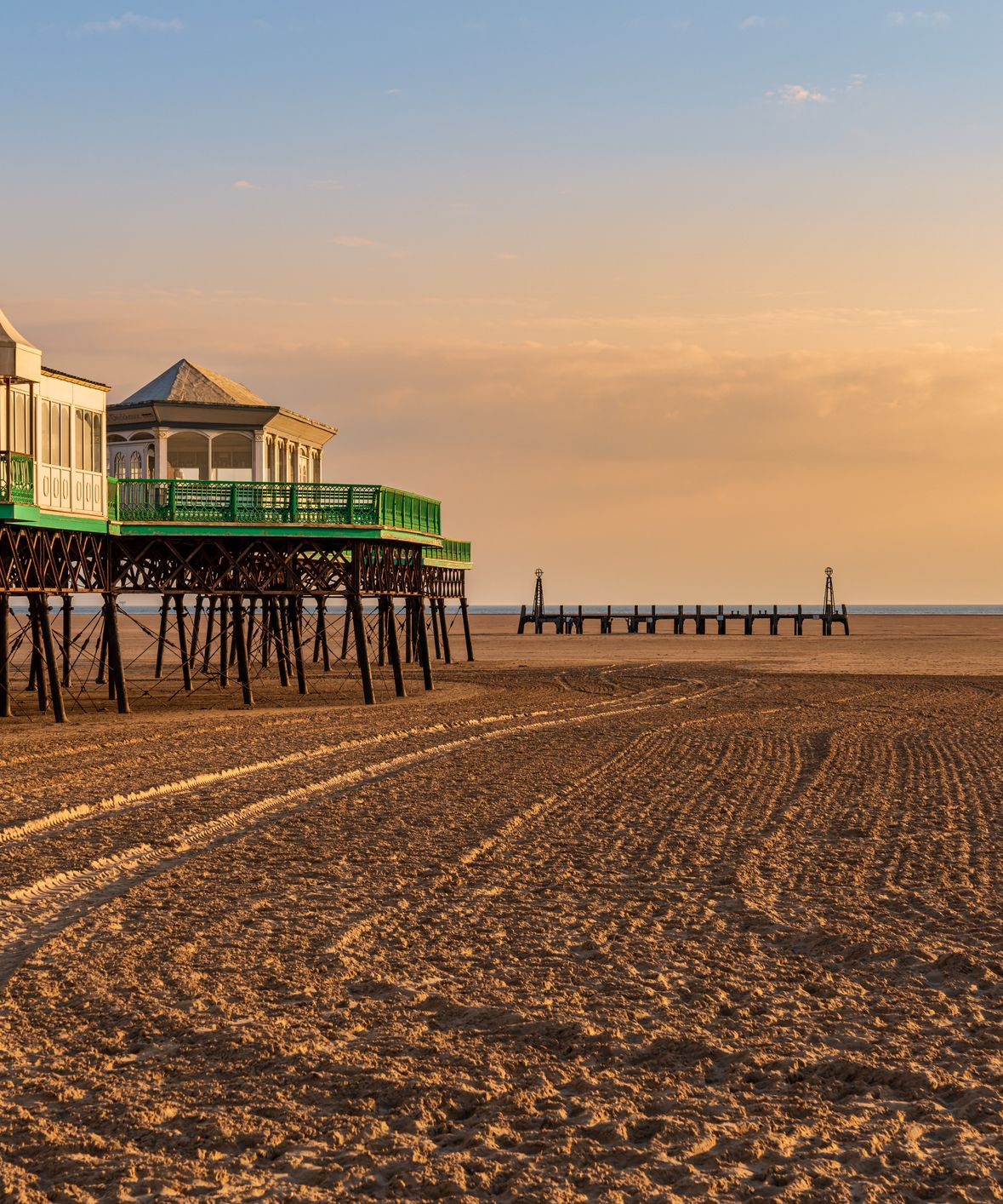 Pier pavilion over a wide sandy beach at sunset with warm golden light and calm sea