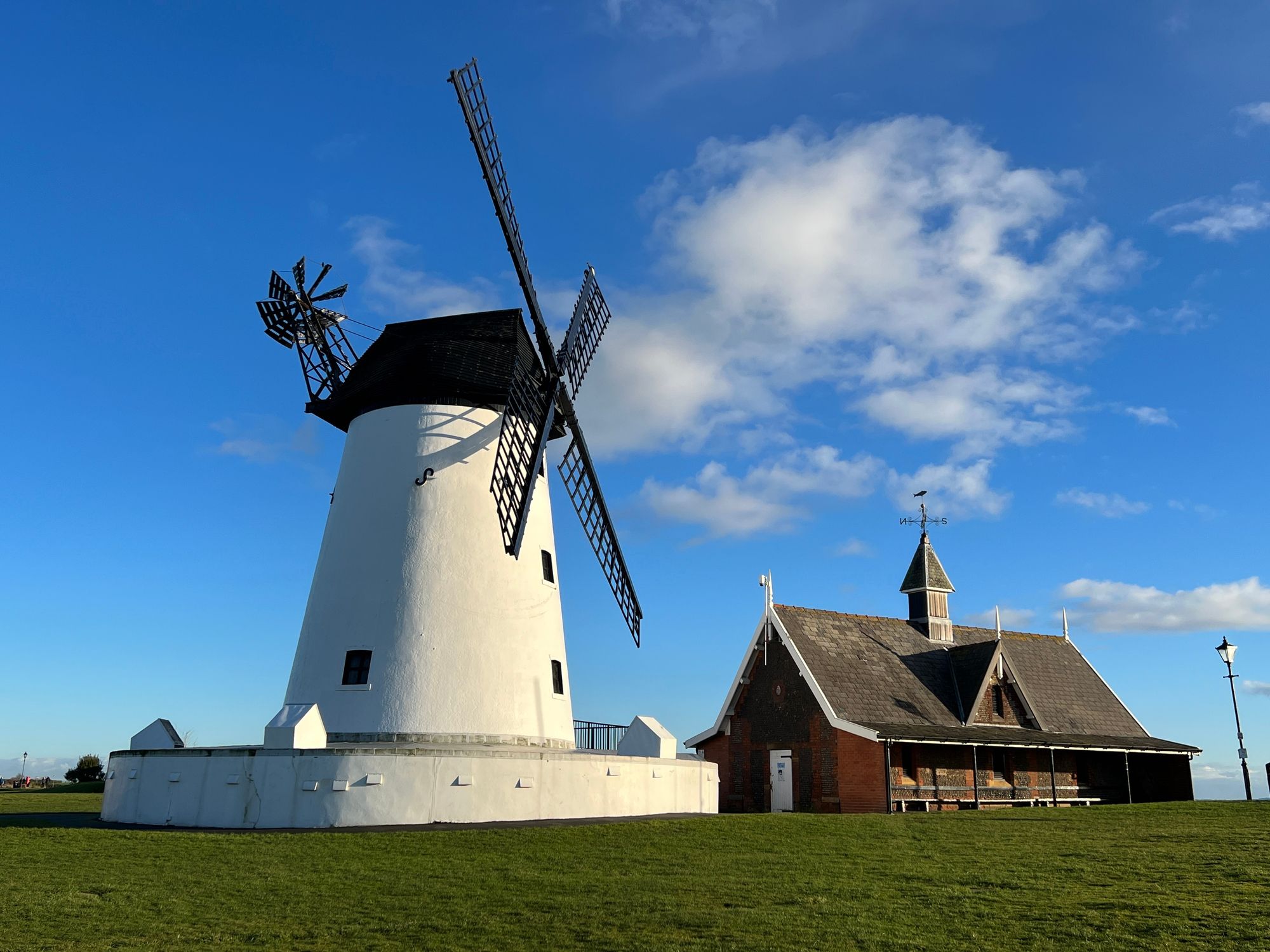 White windmill with black sails beside a brick building under a blue sky