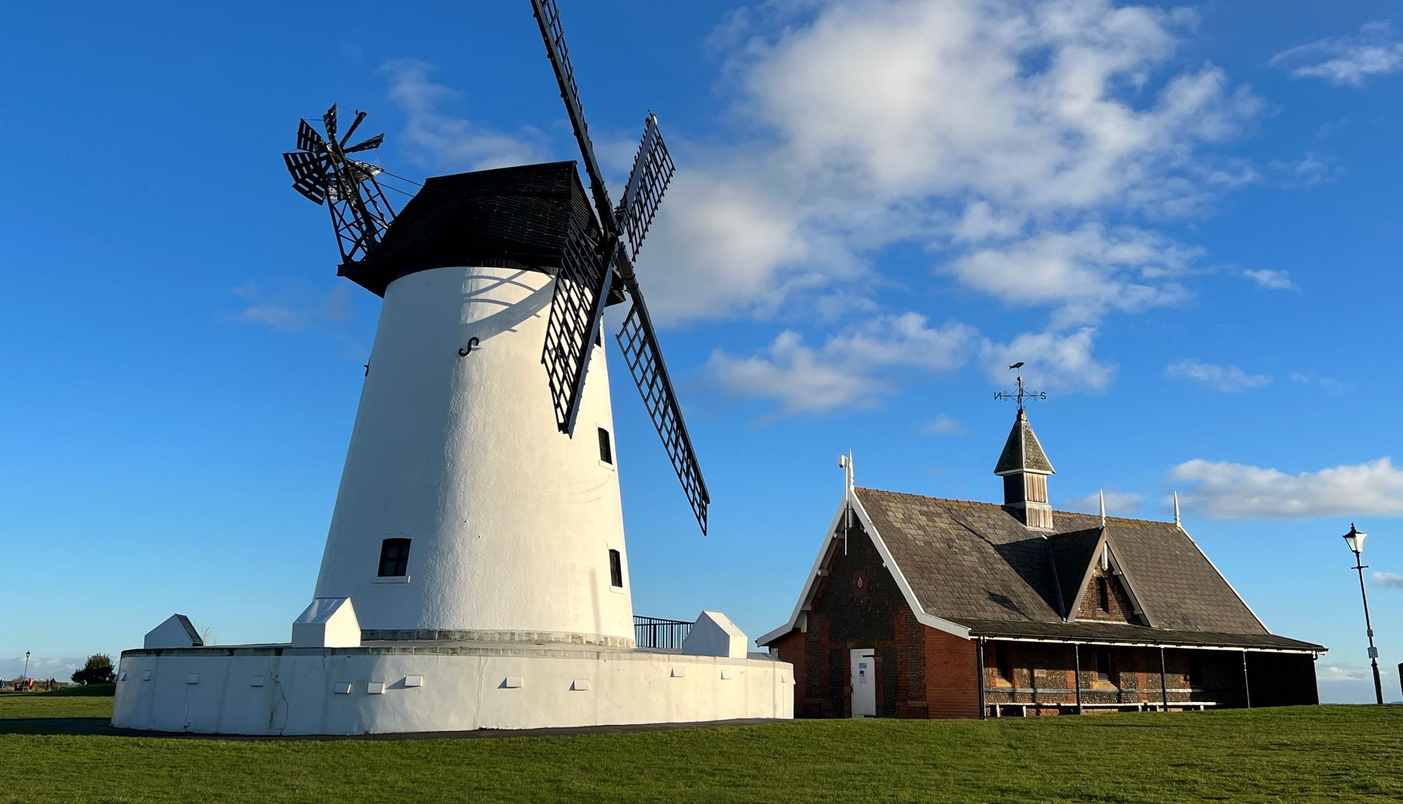 White windmill with black sails beside a brick building under a blue sky