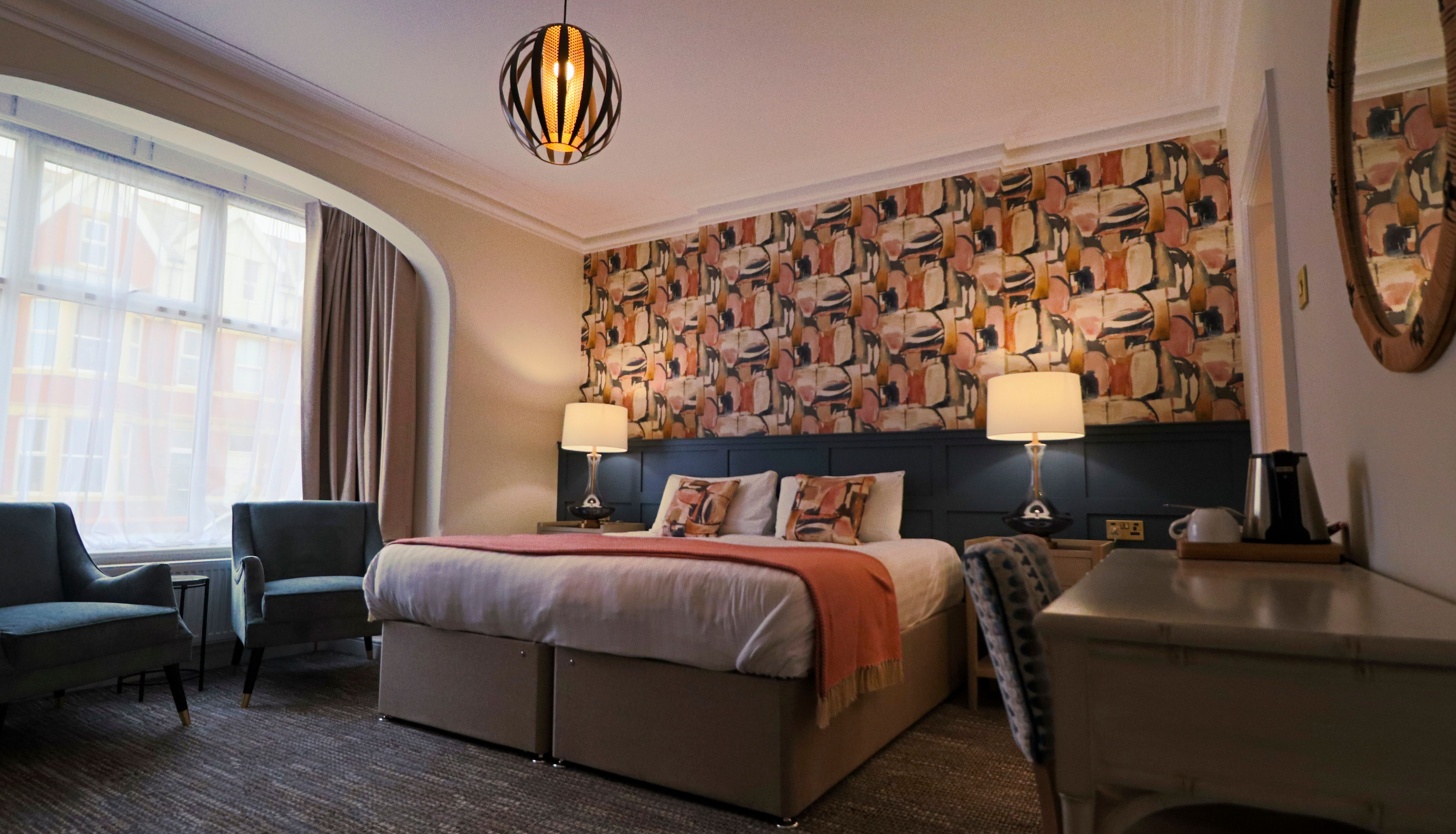 Cosy hotel bedroom with double bed, patterned feature wall, bedside lamps and large bay window