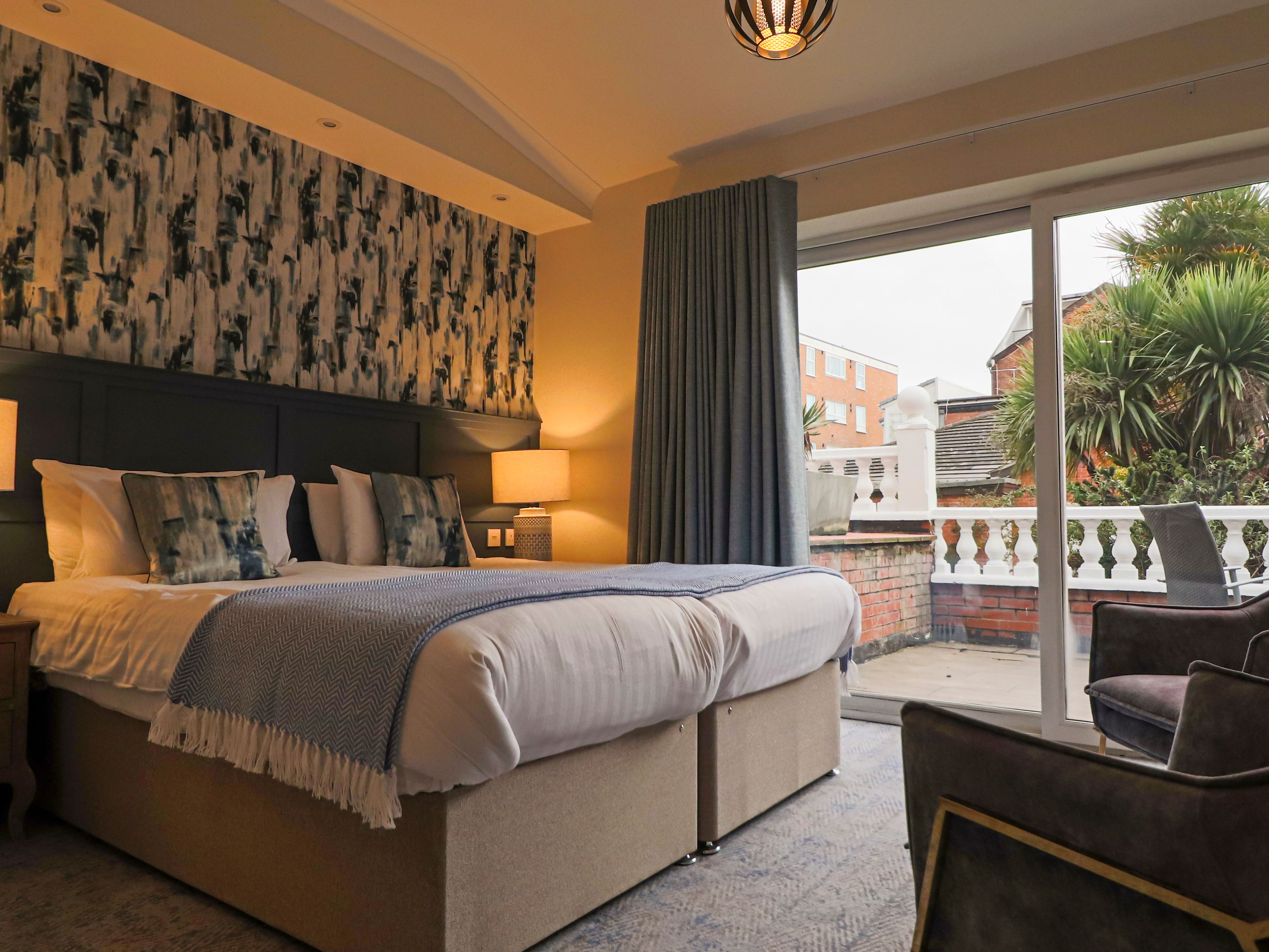 Modern bedroom with double bed, bedside lamps, patterned feature wall and sliding doors to a balcony