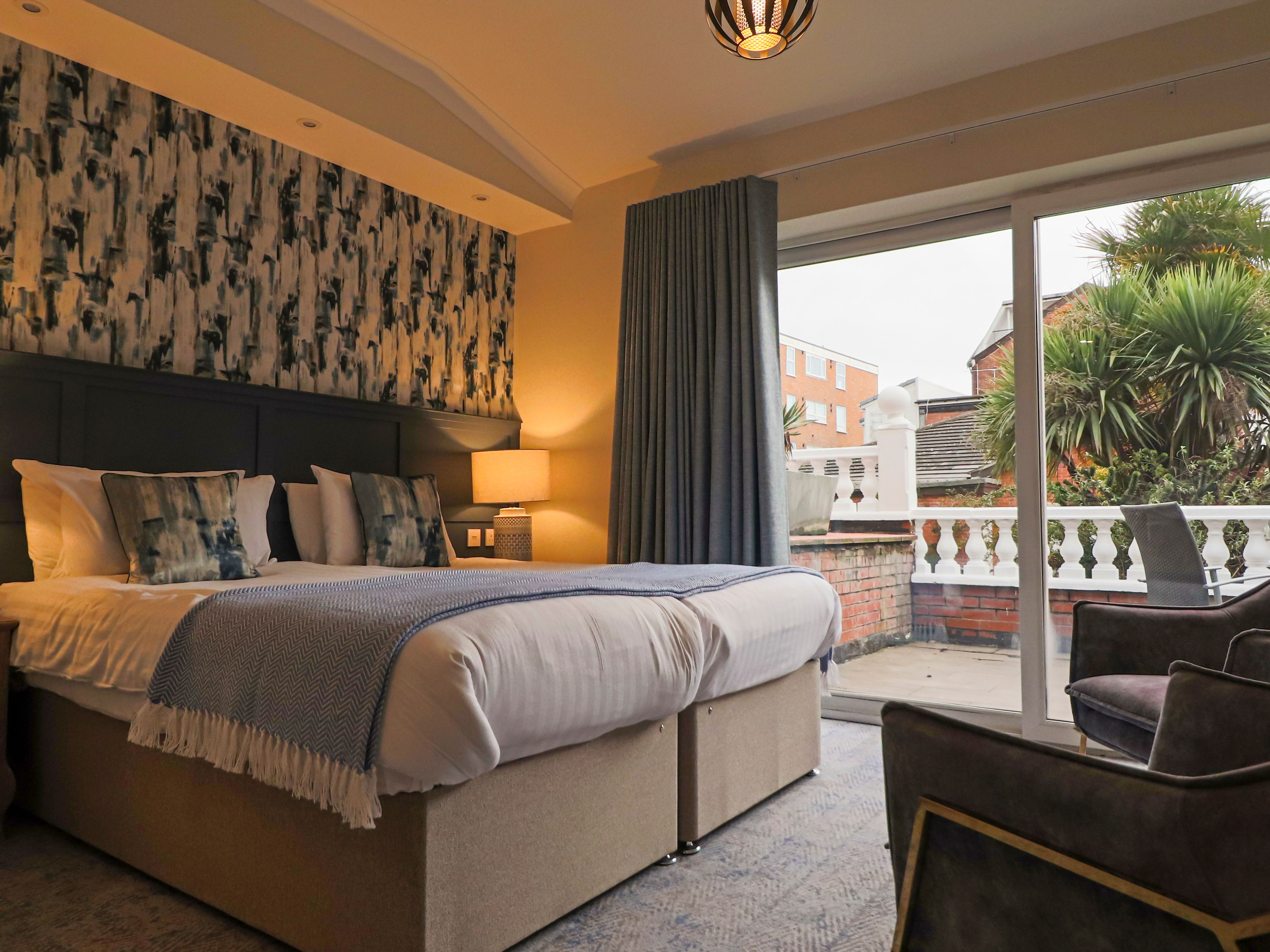 Modern bedroom with double bed, bedside lamps, patterned feature wall and sliding doors to a balcony