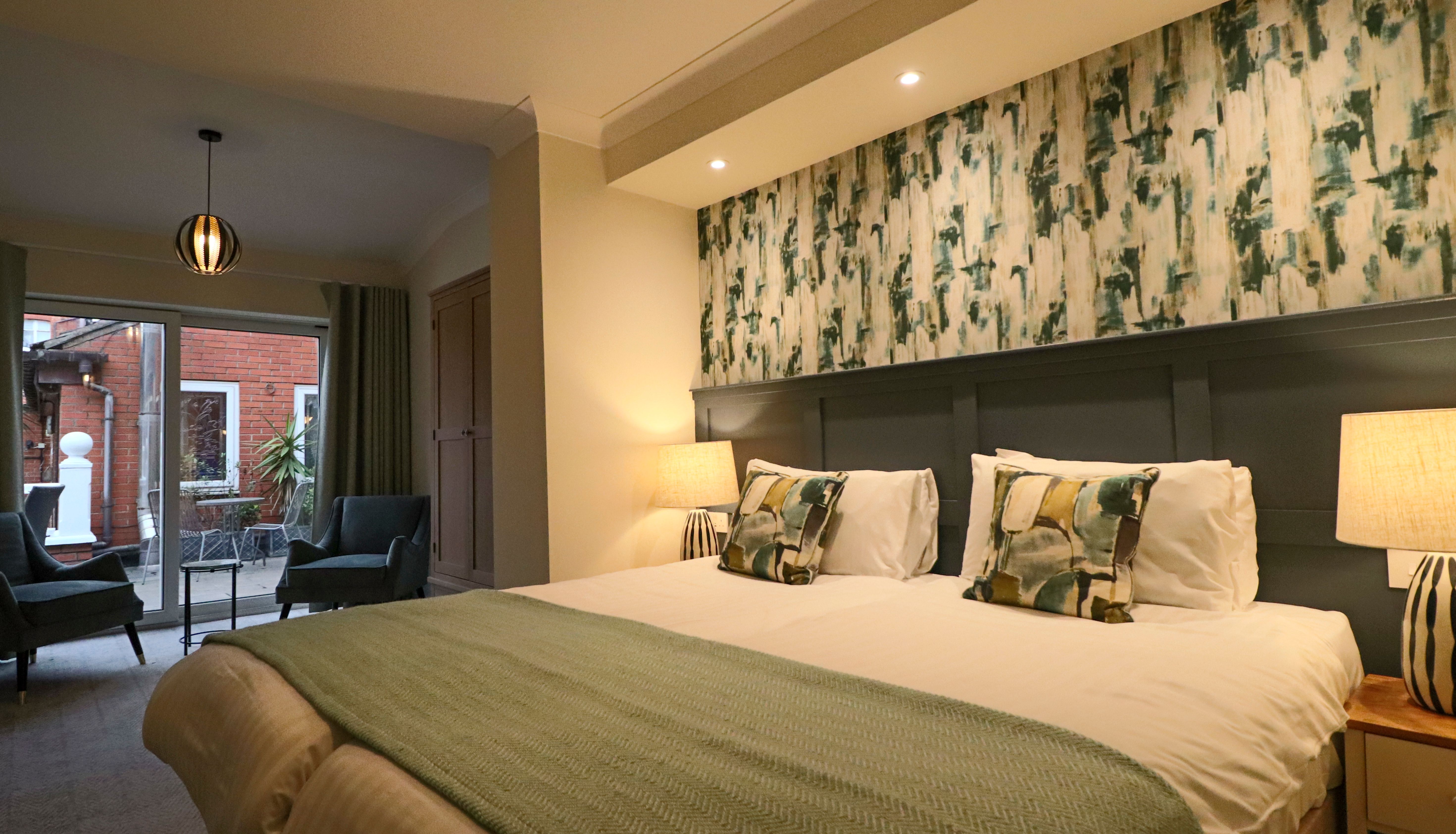 Modern bedroom with double bed, green patterned wallpaper and bedside lamps, opening to a small patio