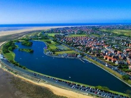 Aerial view of Fairhaven Lake beside the beach, with a coastal town and promenade in the distance.