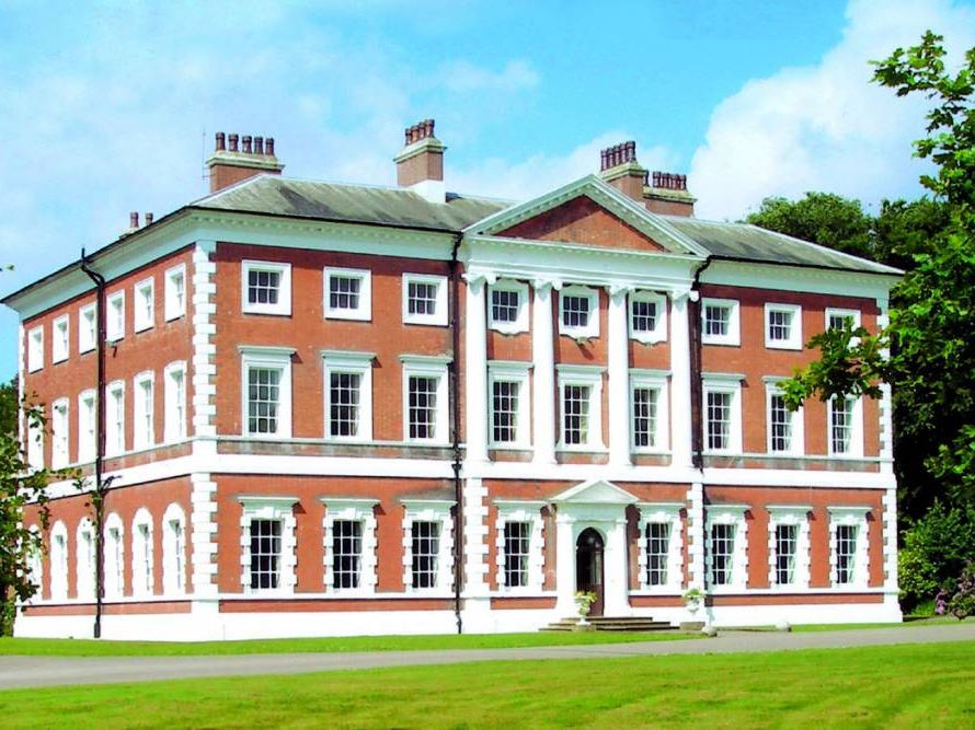 Lytham Hall, a Georgian red-brick country house with white columns and sash windows, set on a green lawn under a blue sky