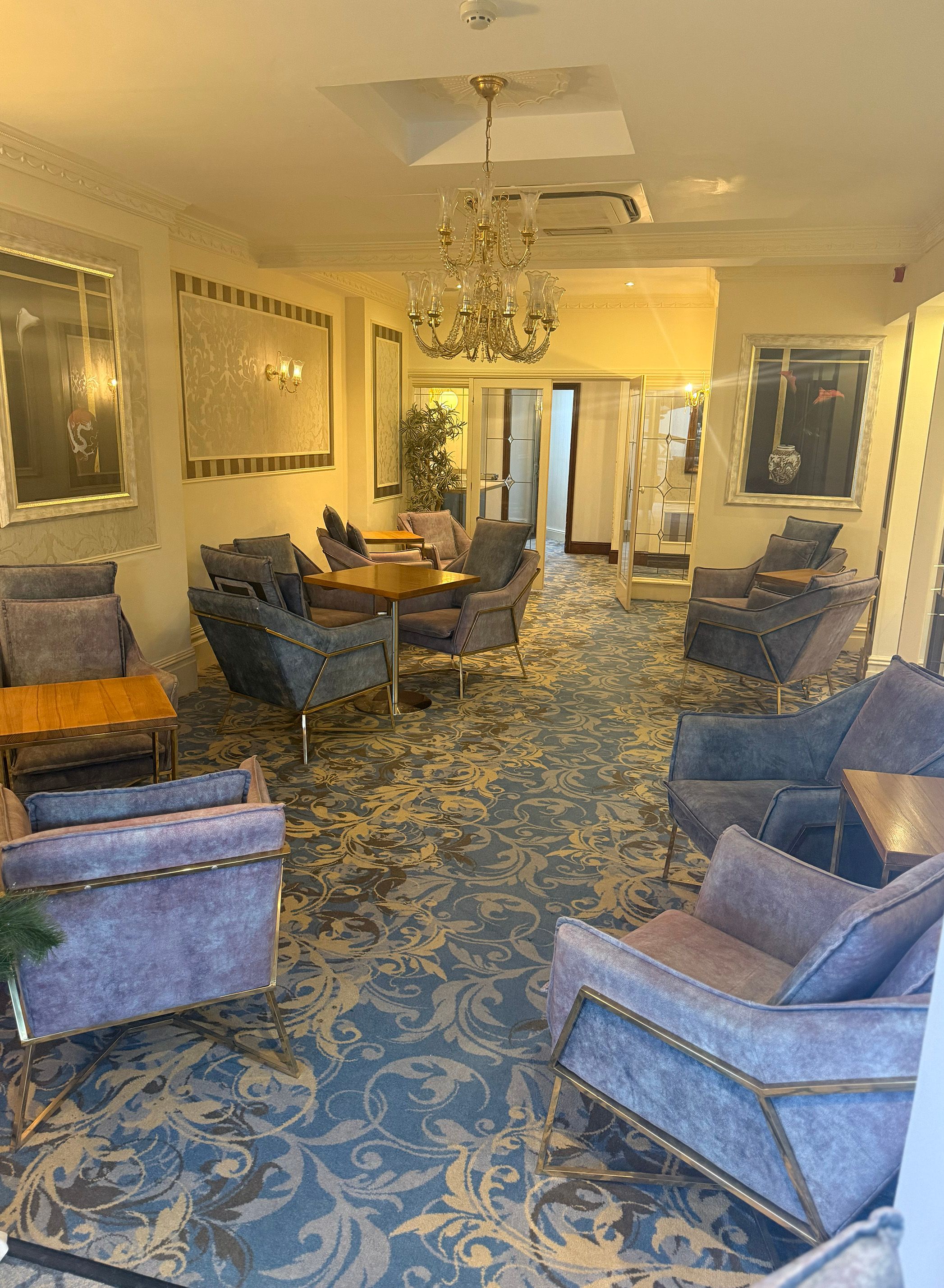 Elegant lounge seating area with blue armchairs, wooden tables and a chandelier