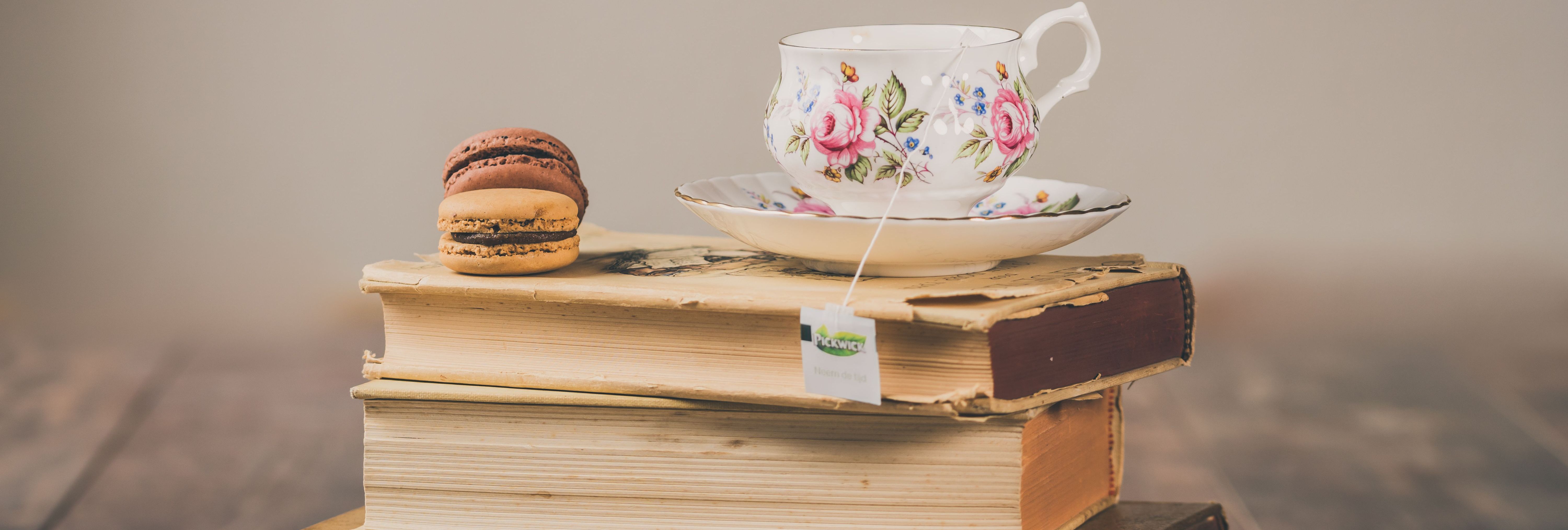 Floral teacup and saucer on a stack of vintage books with two macarons and reading glasses