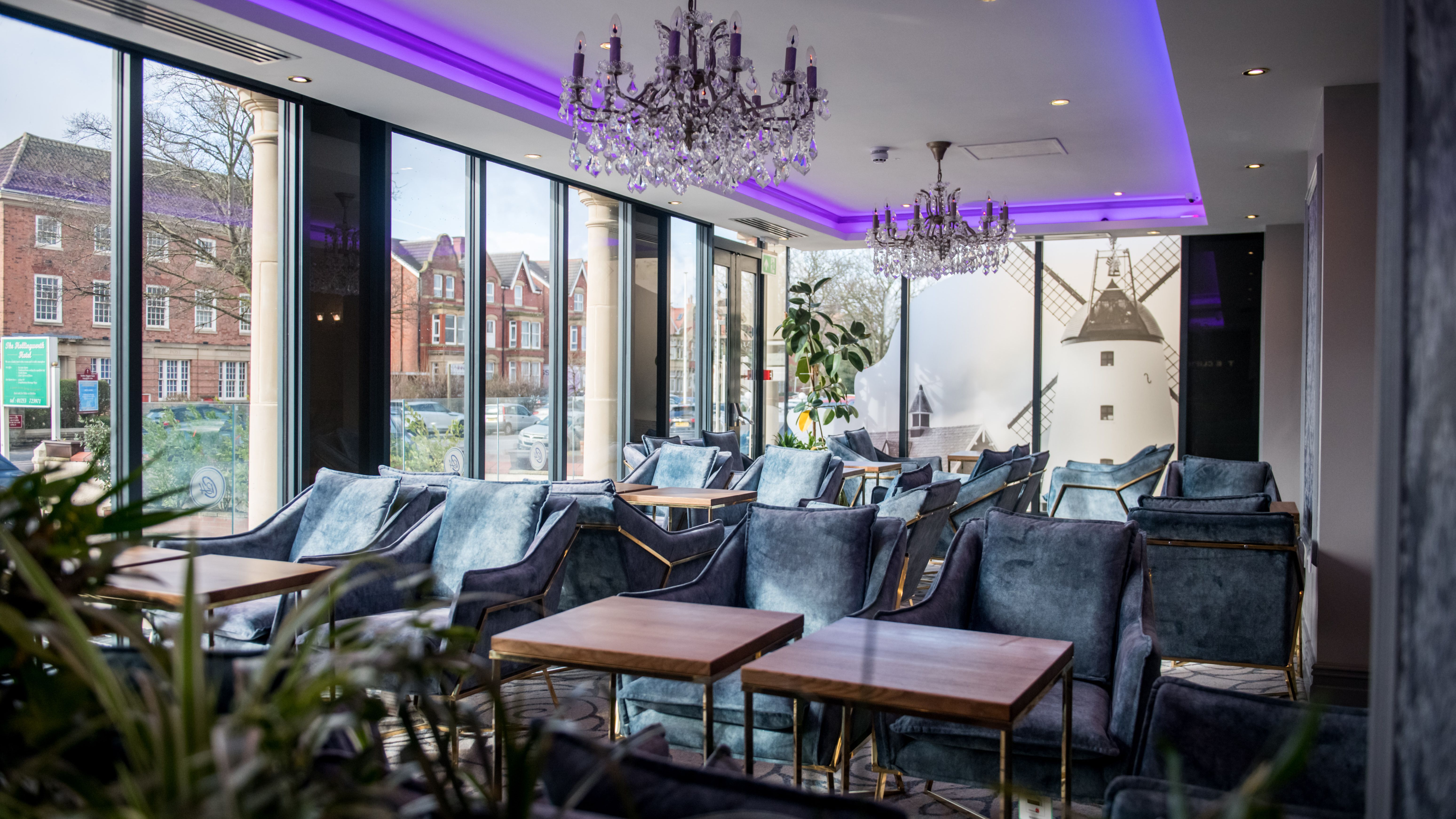 Modern lounge seating area with velvet chairs, wooden tables and crystal chandeliers beneath purple LED ceiling lighting