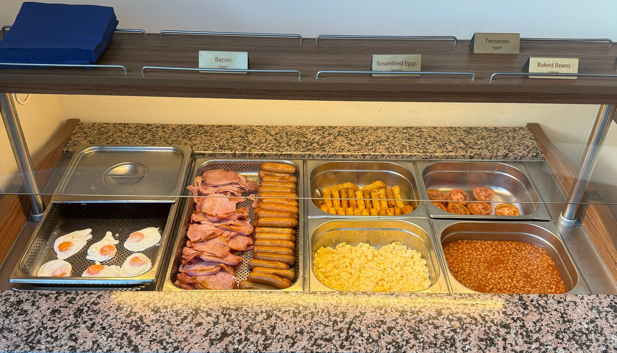 Hot breakfast buffet counter with eggs, bacon, sausages, hash browns, tomatoes and baked beans.
