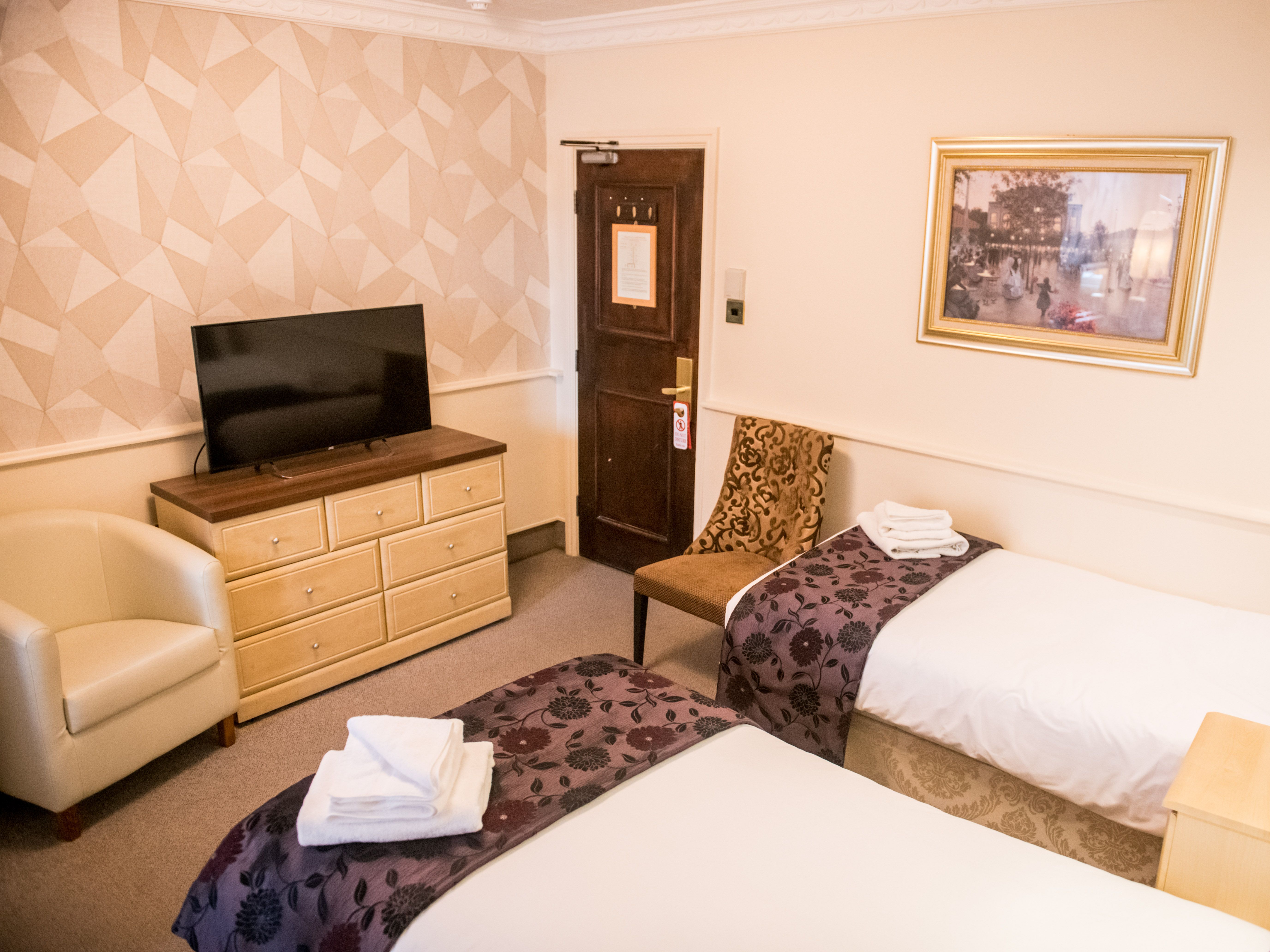 Twin hotel room with two single beds, television on a chest of drawers, and patterned chair