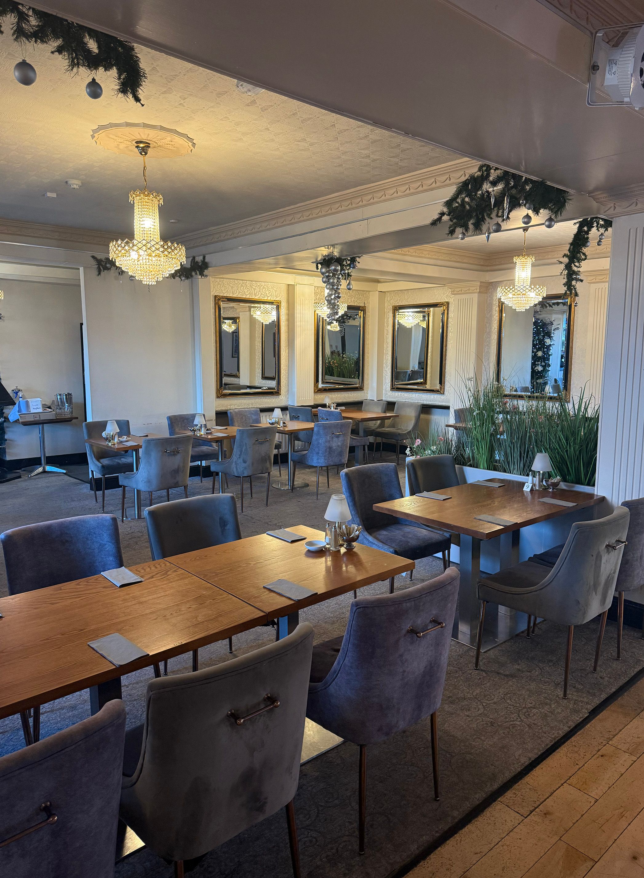 Elegant dining room with wooden tables, grey velvet chairs, chandeliers and festive garlands