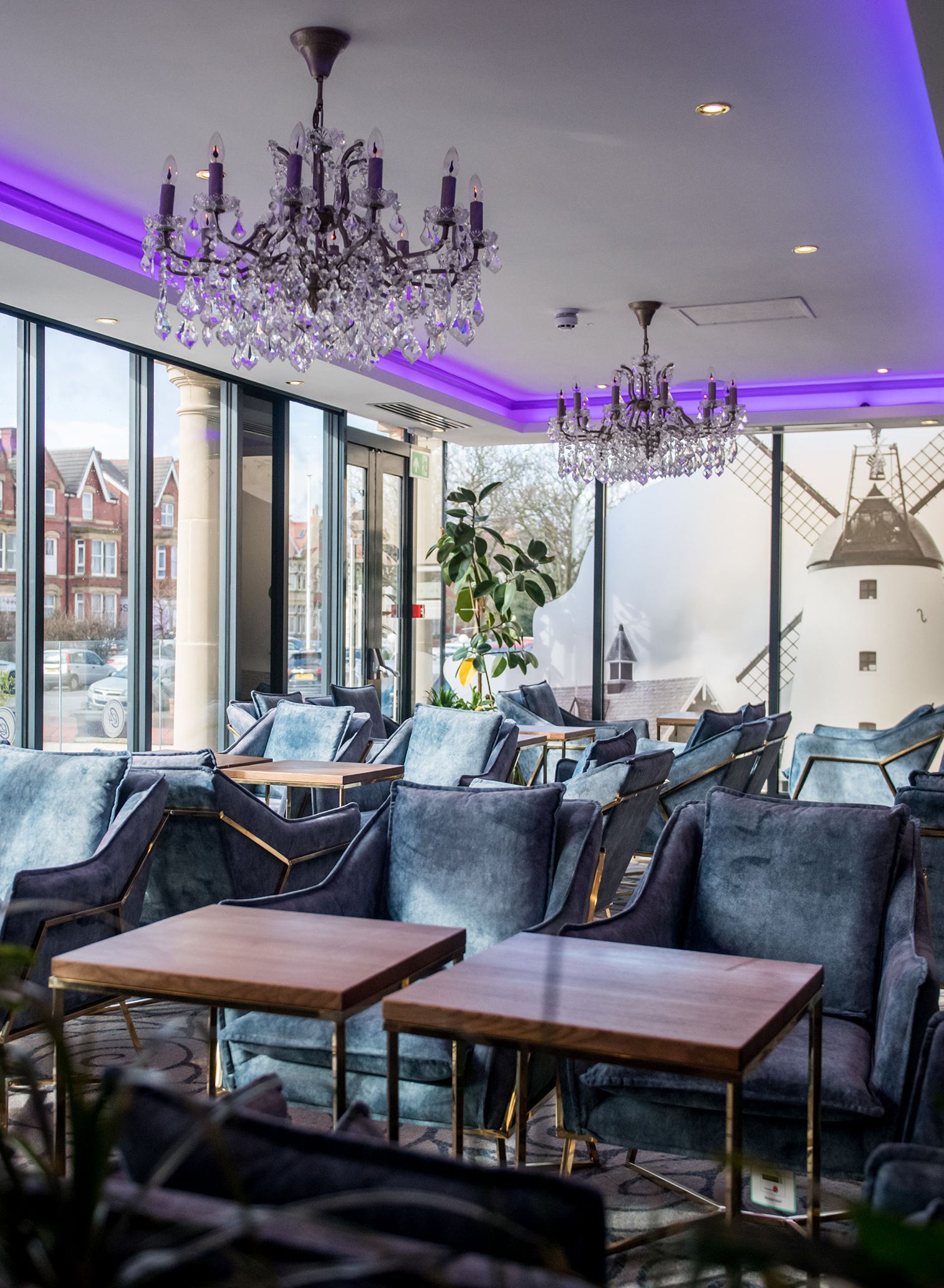 Modern lounge area with velvet armchairs, wooden tables and crystal chandeliers under purple LED lighting